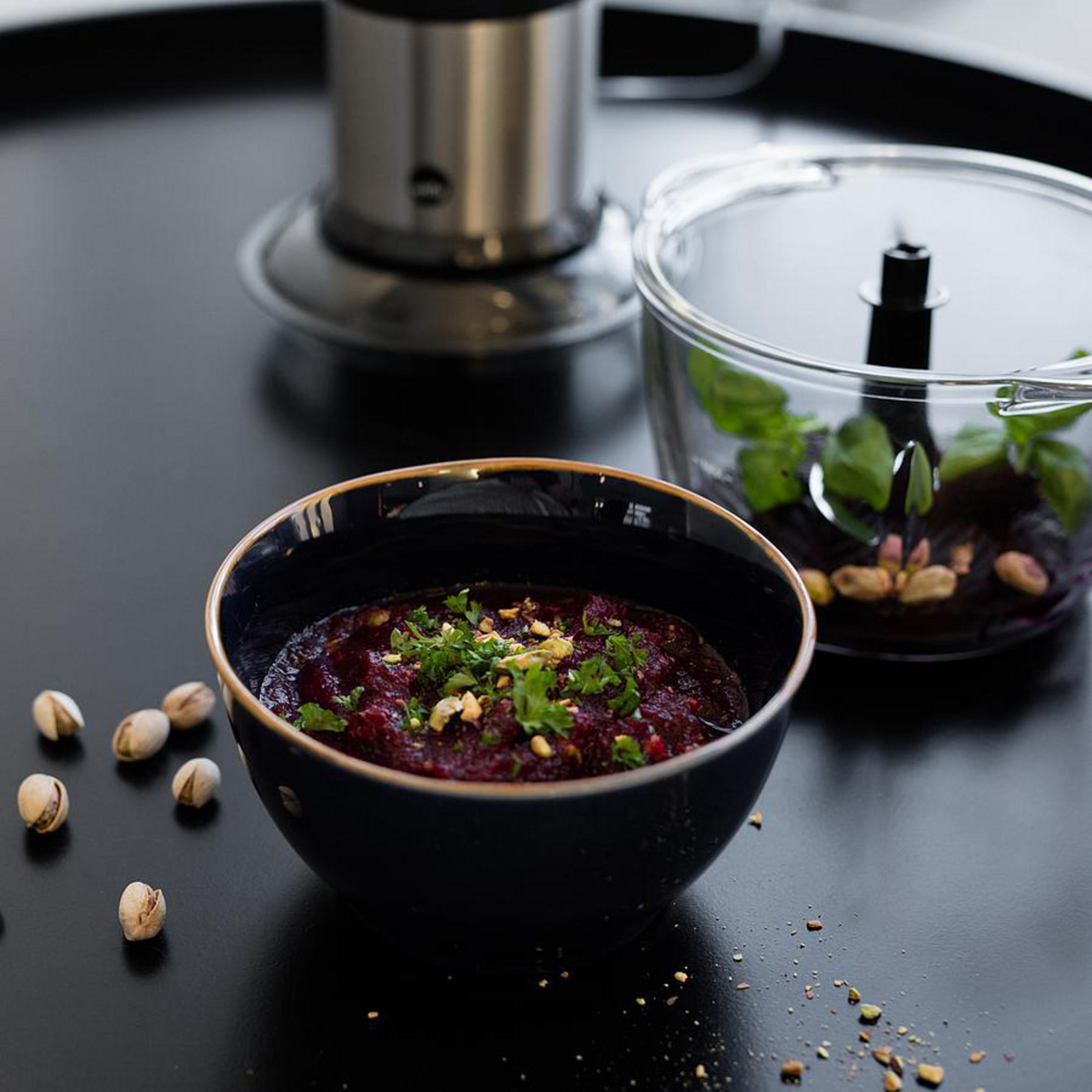 Eine Schüssel mit Rote-Bete-Püree mit Pistazien und Kräutern, auf schwarzem Untergrund, im Hintergrund.