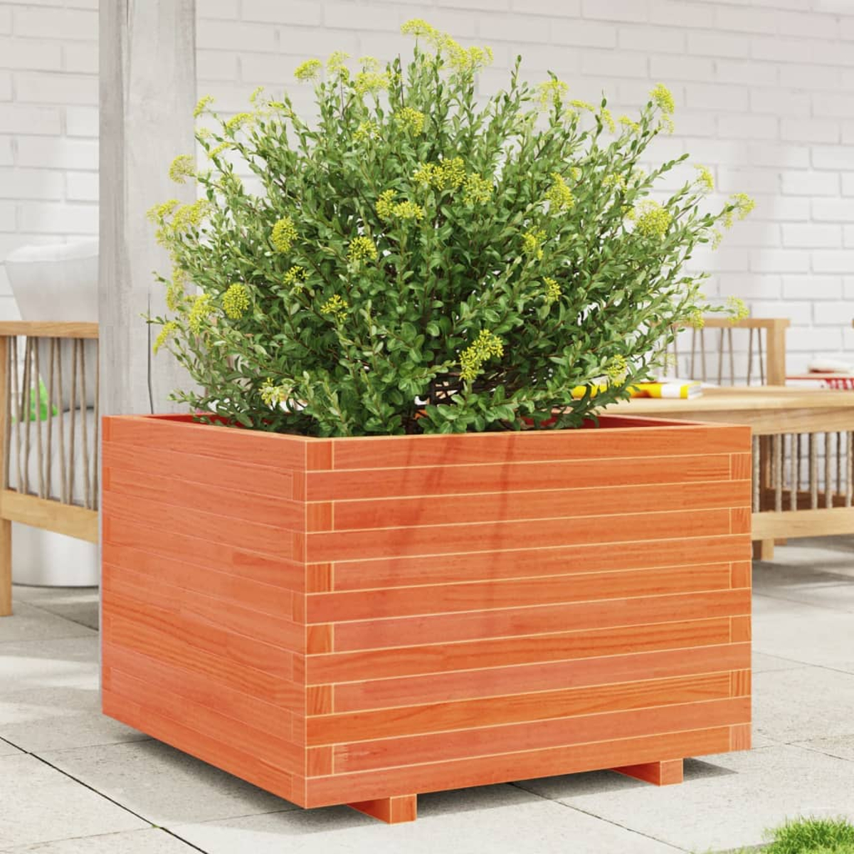 Holzpflanzkübel mit grünen Pflanzen und gelben Blumen vor einer weißen Backsteinmauer.