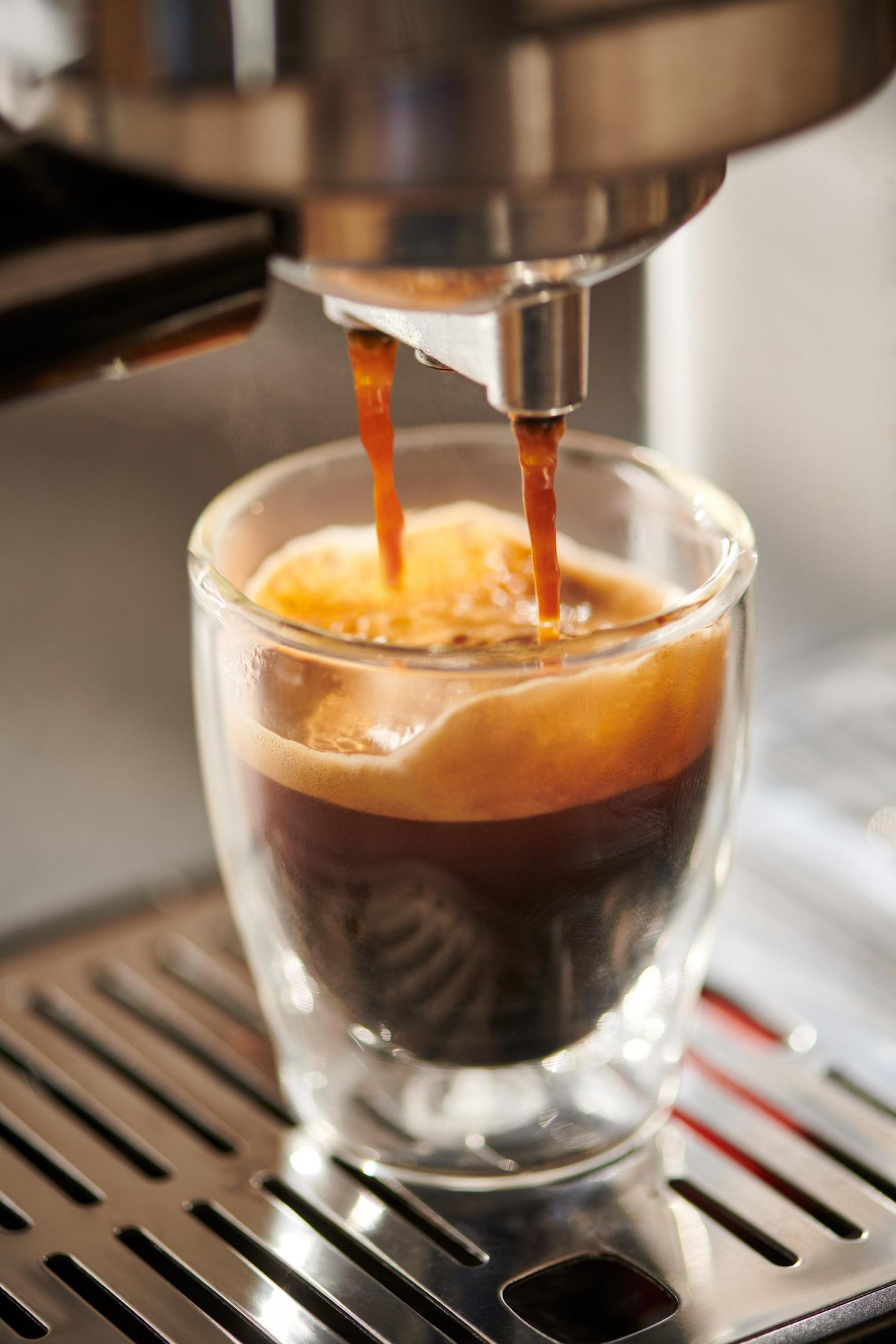 Espressomaschine gießt Kaffee in ein Glas. Brauner Kaffee mit Schaum.