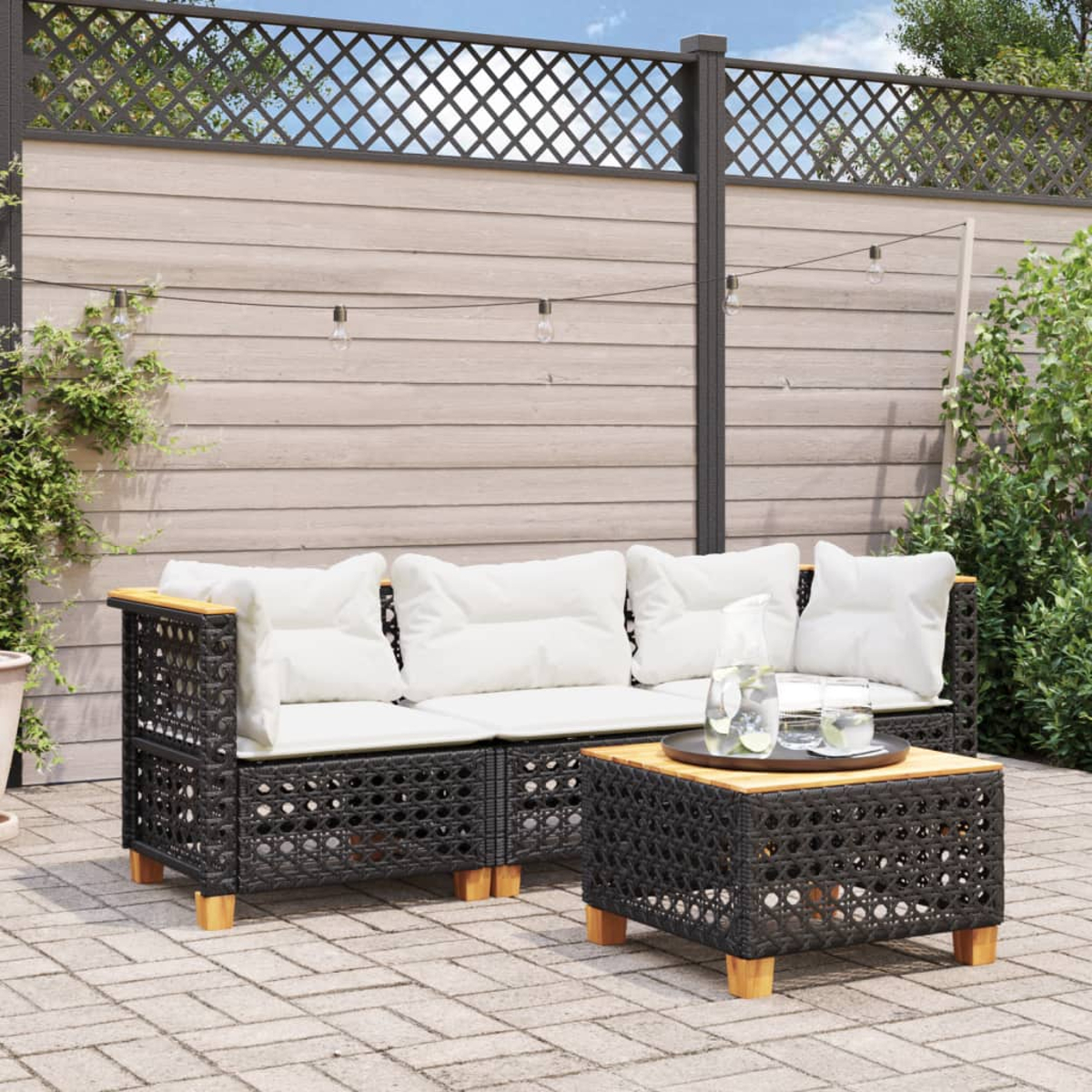 Outdoor-Sitzbereich mit schwarzem Korbmöbel, Holztisch und weißen Kissen. Sonniger Tag.