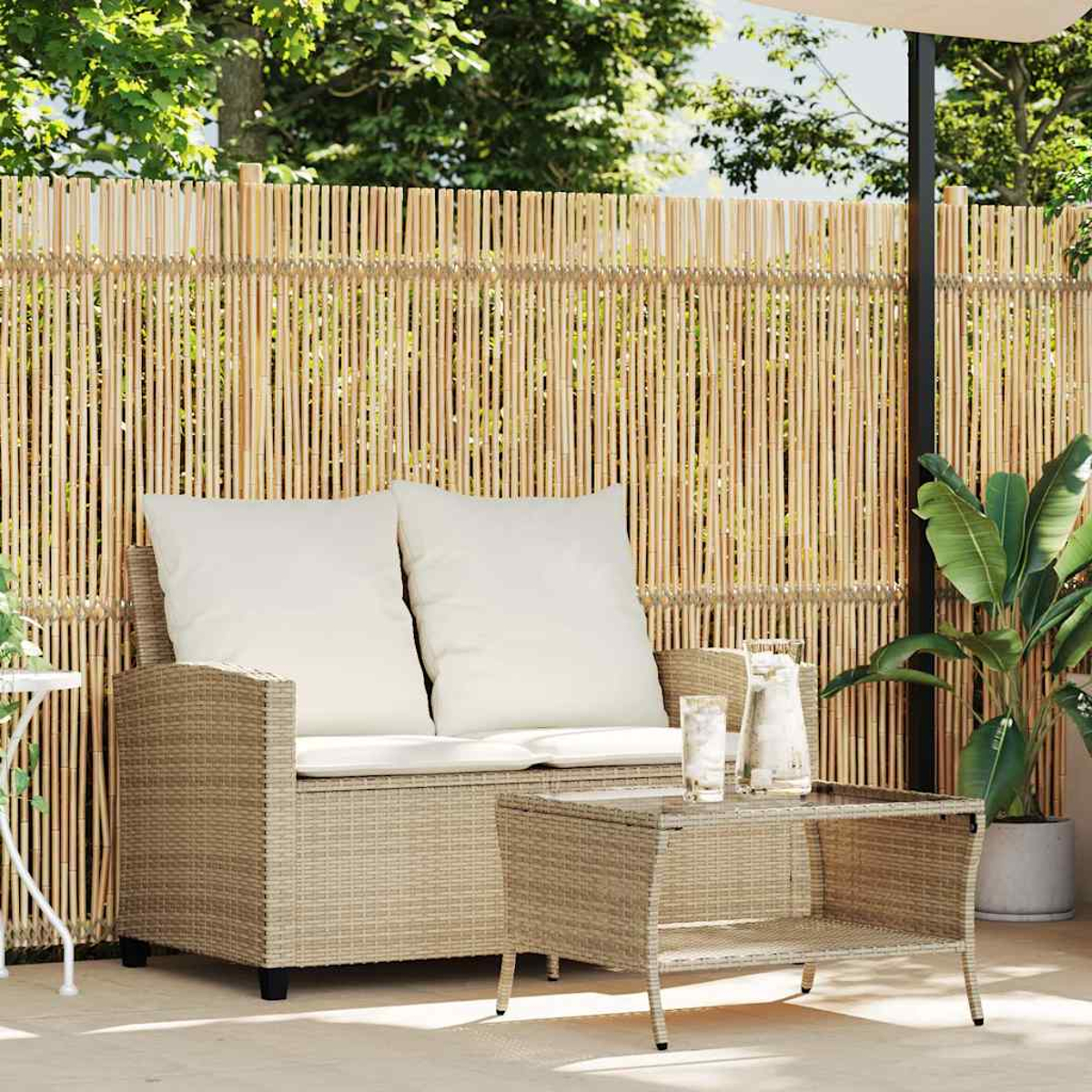 Divanetto in vimini beige con due cuscini bianchi e tavolino coordinato su un patio.