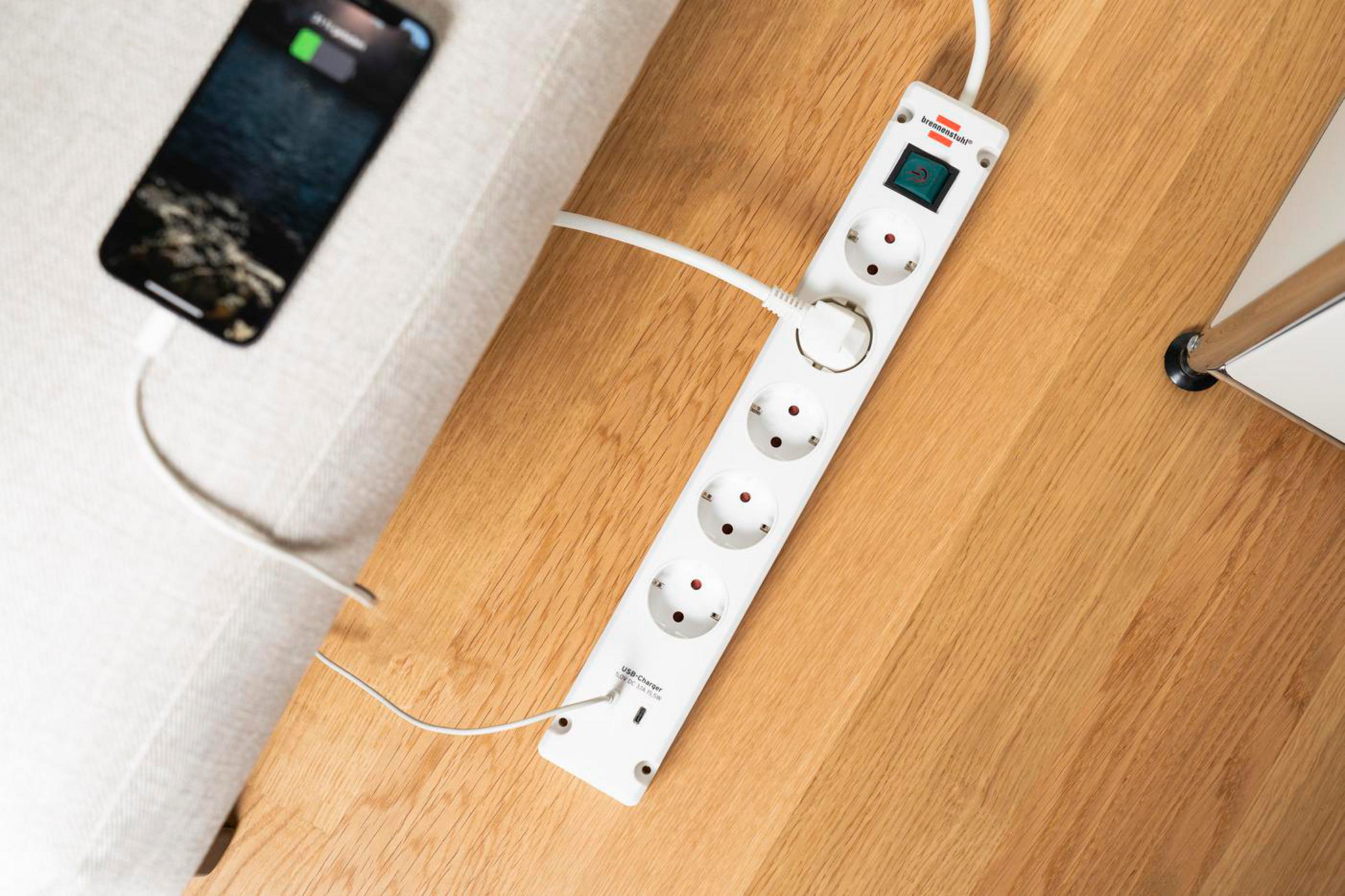 Telefon ładujący się na drewnianym stole z białą listwą zasilającą z 6 gniazdami.