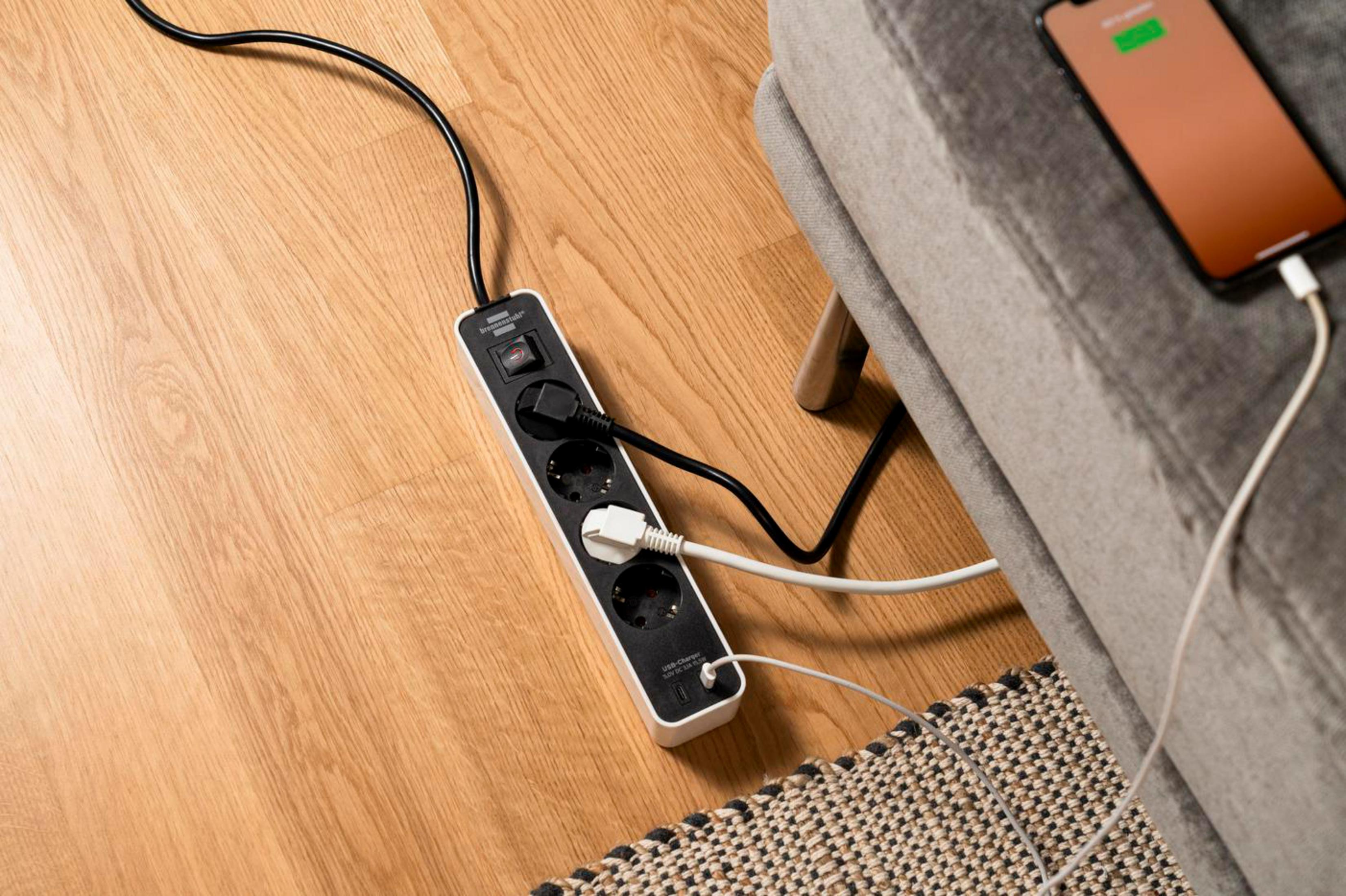 Czarna listwa zasilająca z wieloma gniazdami i ładowarką USB. Telefon ładuje się z boku.