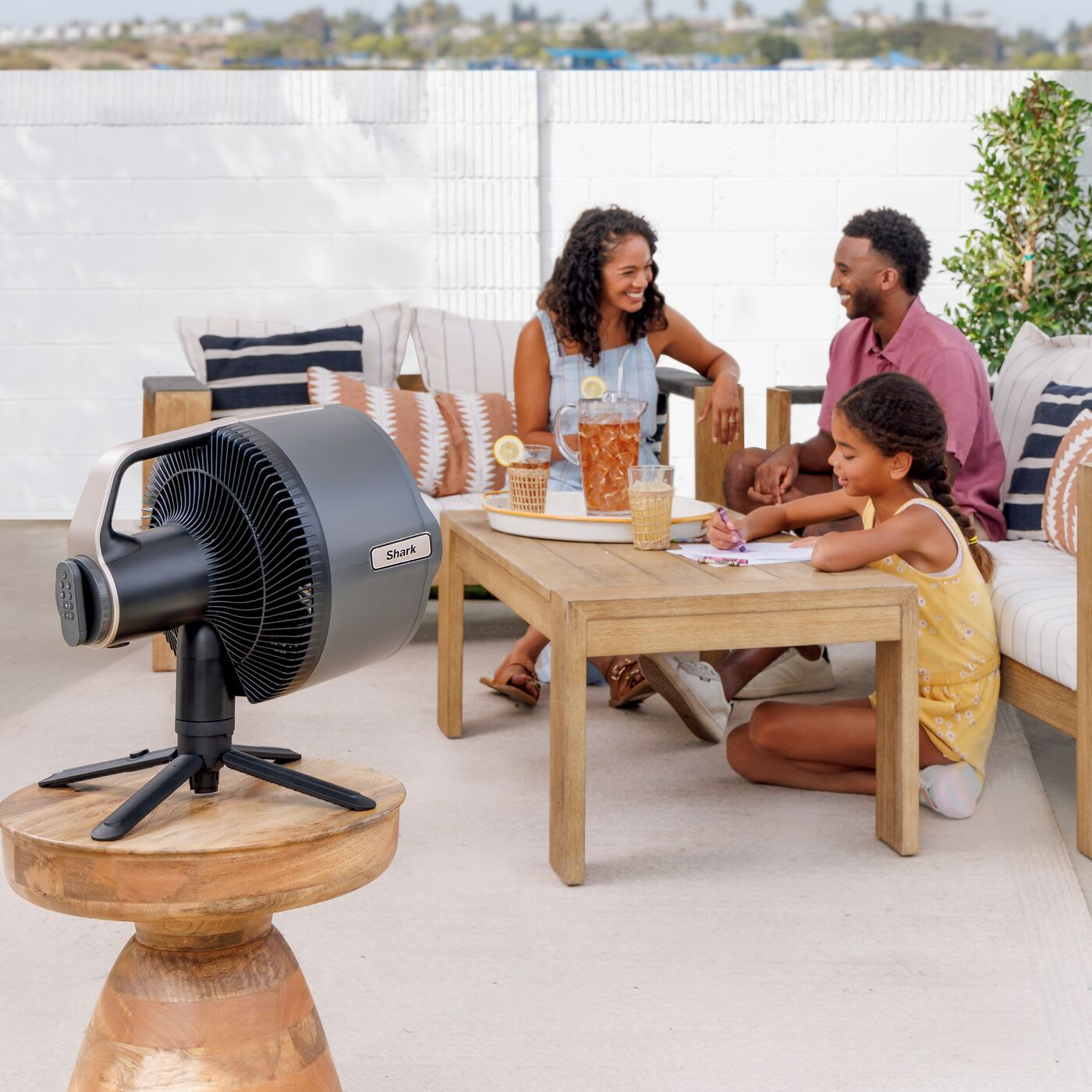 Rodzina na zewnątrz. Widoczny wentylator, stół i ludzie. Scena jest jasna i słoneczna.