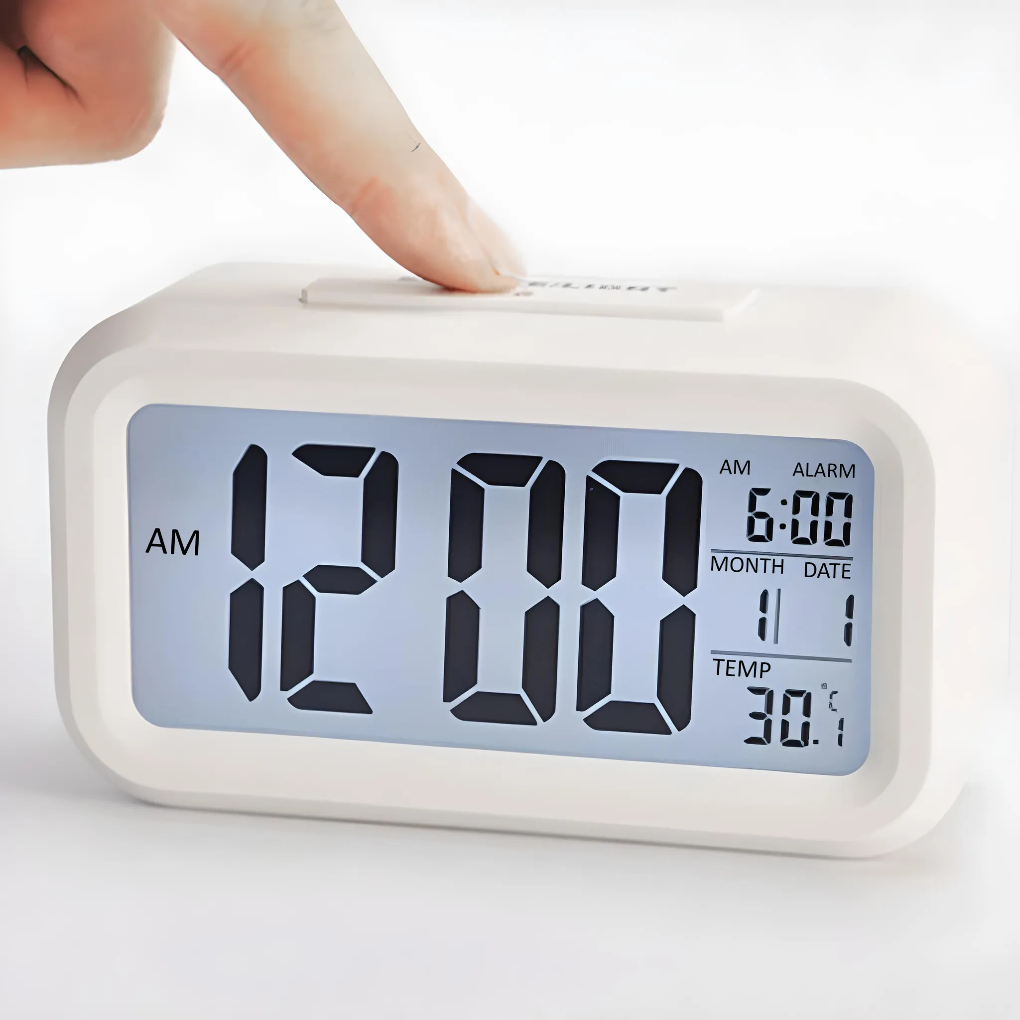 Weißer digitaler Wecker mit der Anzeige 12:00 AM. Ein Finger drückt die obere Taste des Weckers.