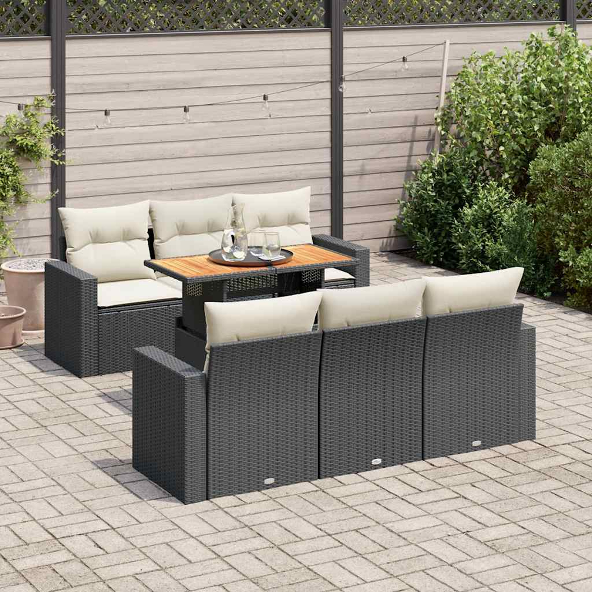Set divano in vimini grigio da esterno con cuscini color crema e tavolo in legno, su un patio in mattoni.