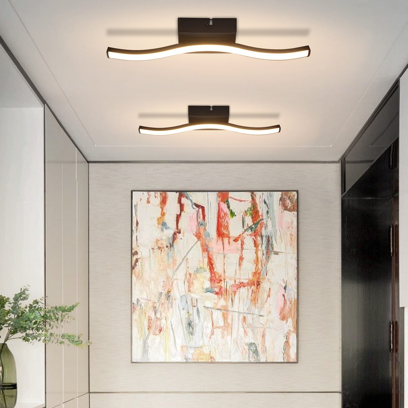 Due lampade a soffitto curve illuminano un corridoio con arte astratta e pareti bianche.
