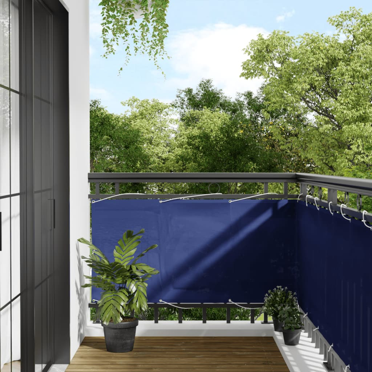 Balkon mit blauem Sichtschutz, Pflanzen und Blick auf Bäume unter blauem Himmel.