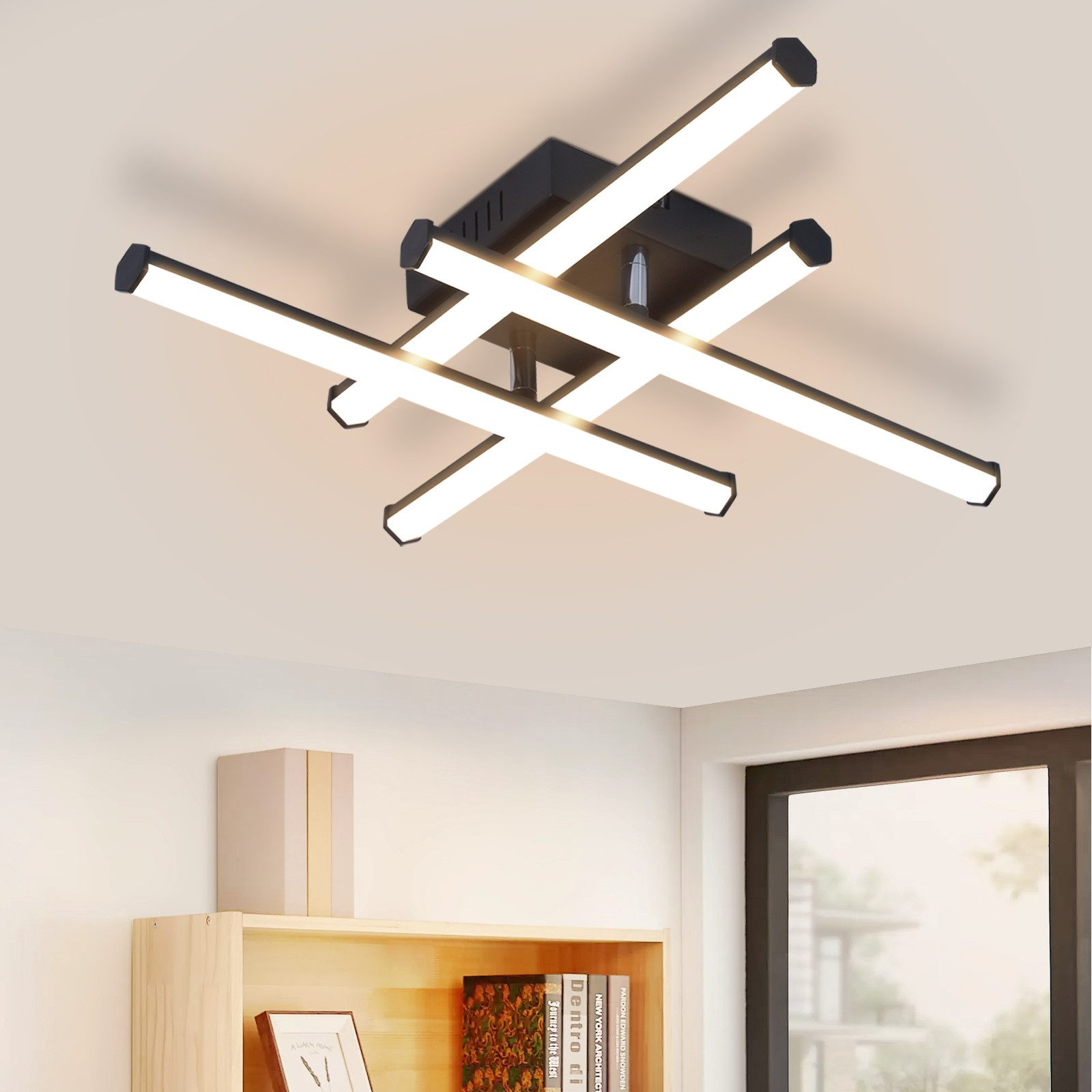 Lampada da soffitto con design nero a croce, le luci sono accese. Sotto, una mensola con libri.