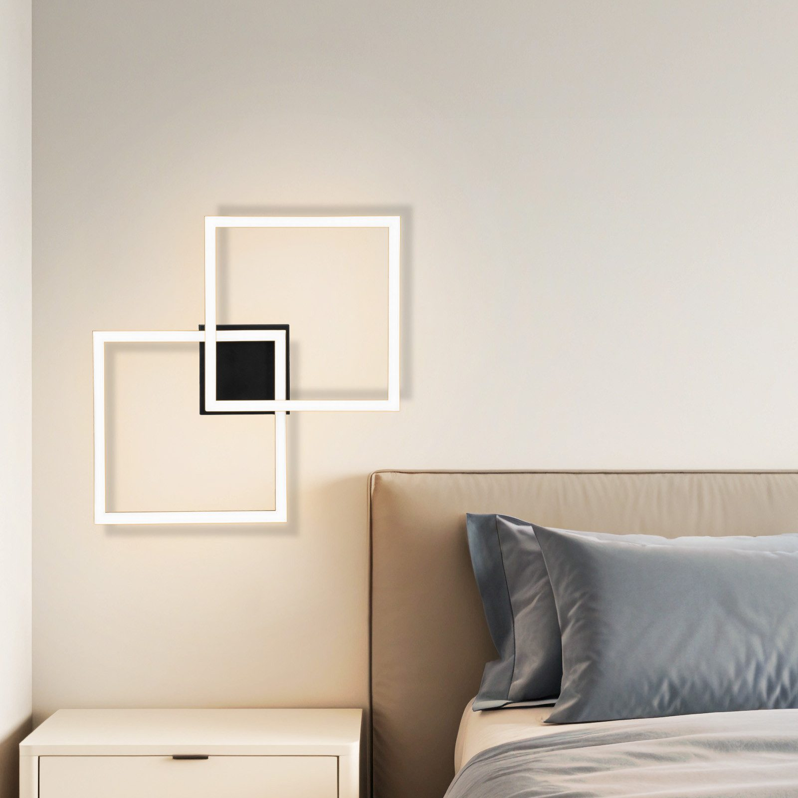 Lampada da parete moderna con quadrati bianchi sovrapposti e centro nero, vicino al letto.