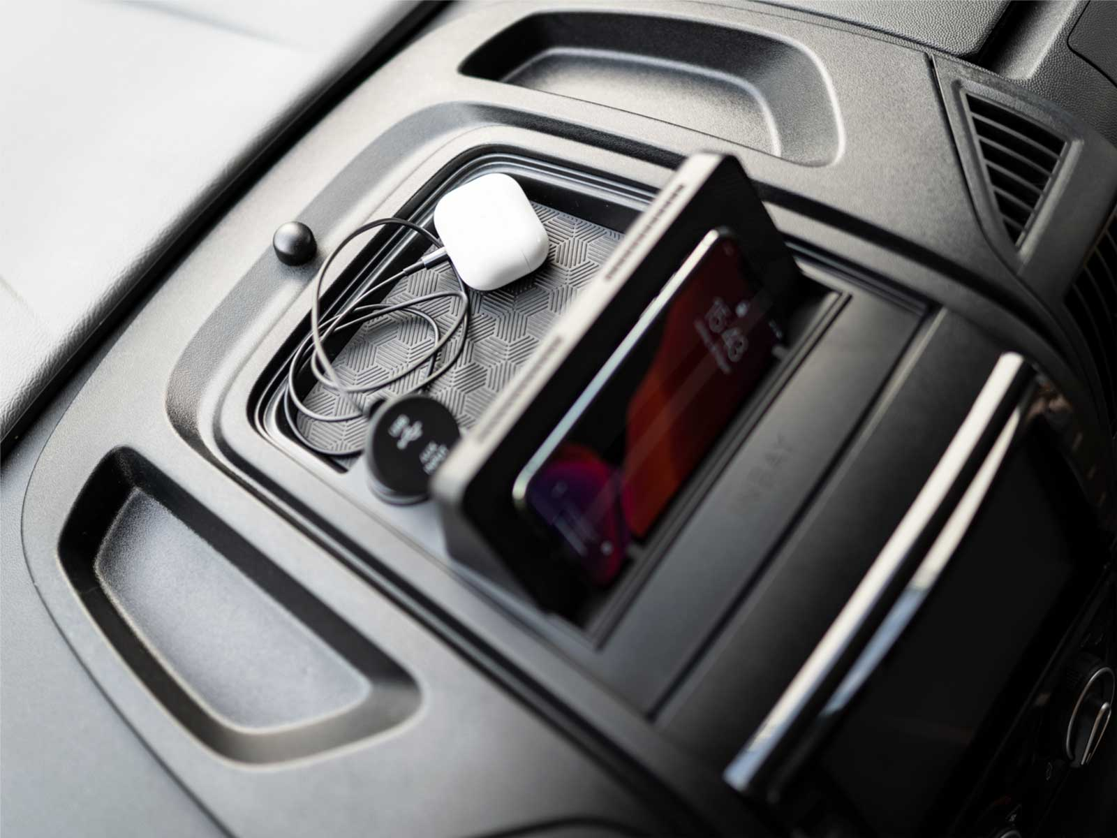 Ein Telefon und Ohrhörer in der Konsolenablage eines Autos. Schwarze Konsole, Telefon zeigt Oberfläche.