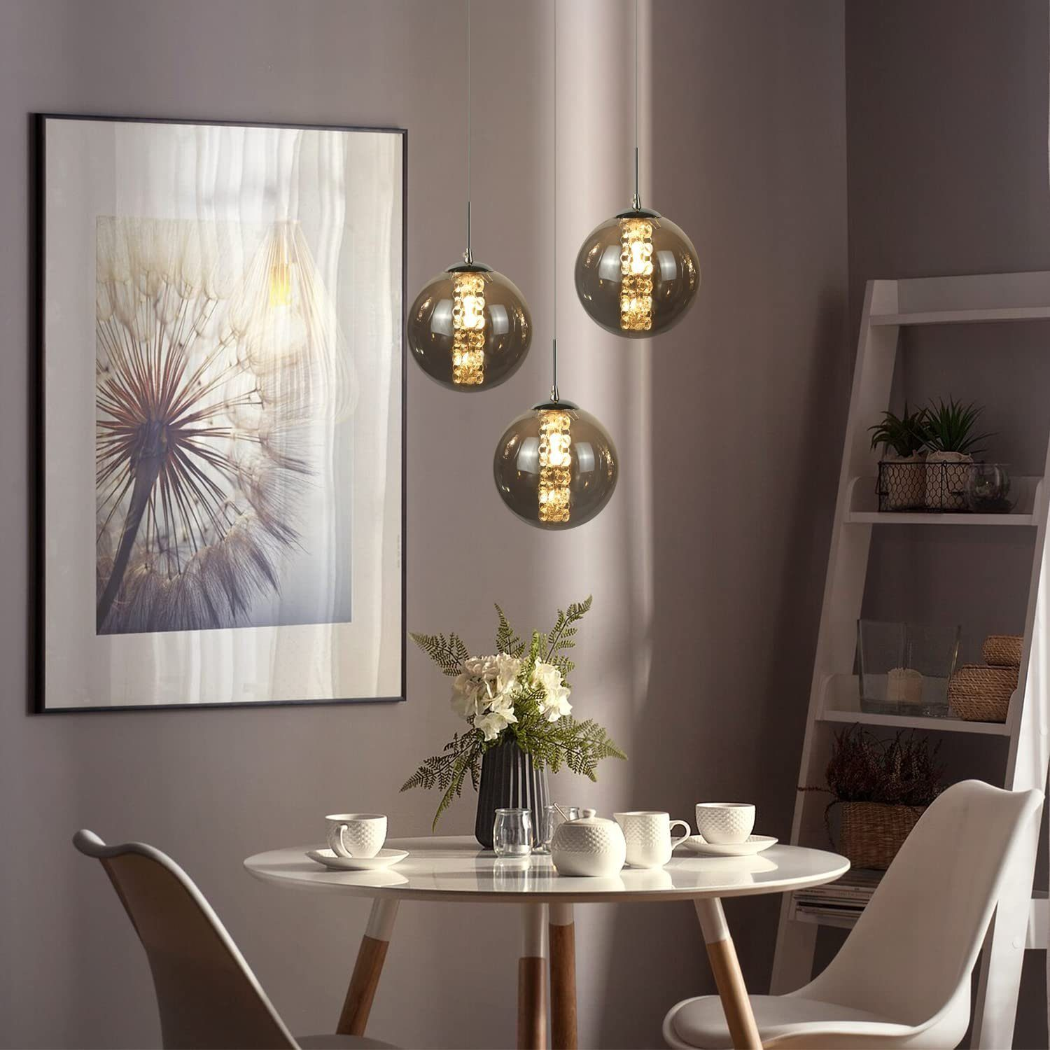 Drei Kugelleuchten hängen über einem Tisch mit Blumen, Tassen und einem gerahmten Bild.