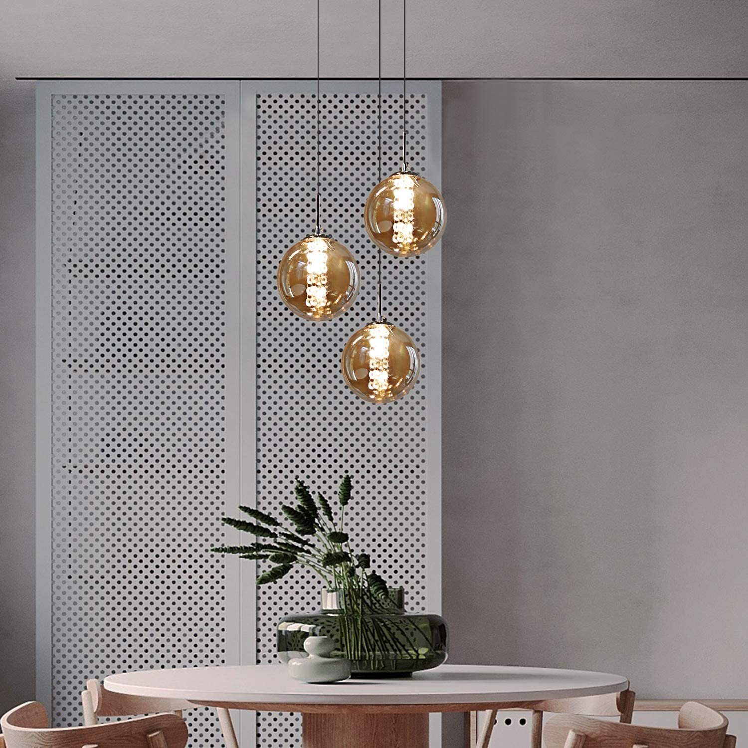 Wiszące lampy z trzema bursztynowymi szklanymi kulami, nad stołem. Pokój ma minimalistyczny design.
