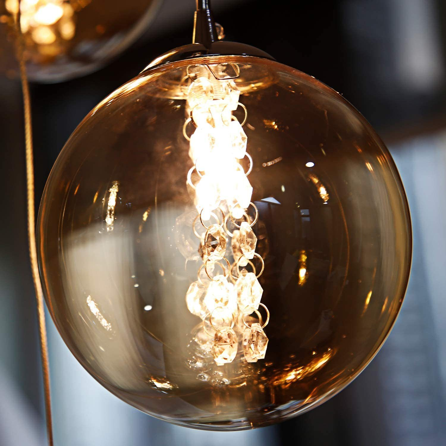 Przezroczysta szklana lampa kulista z łańcuchem kryształów w środku. Światło jest włączone.