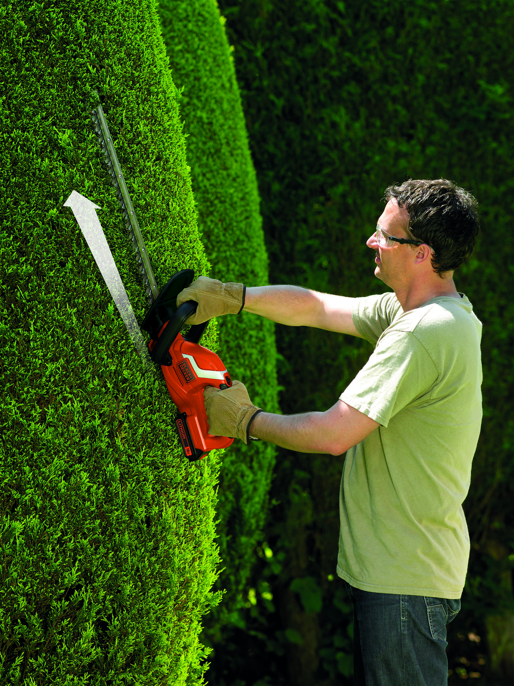 Mężczyzna używa nożyc do żywopłotu na zielonym żywopłocie. Ma rękawice i okulary.