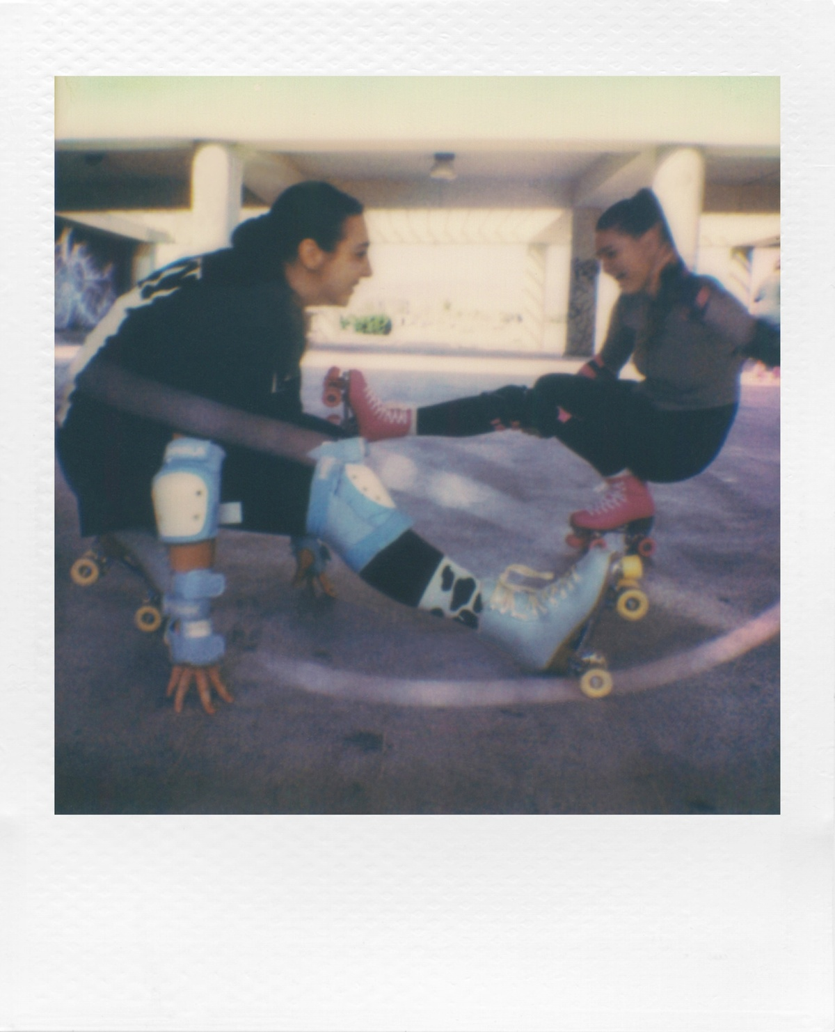 Dos mujeres en patines, una sostiene la pierna de la otra mientras patinan.