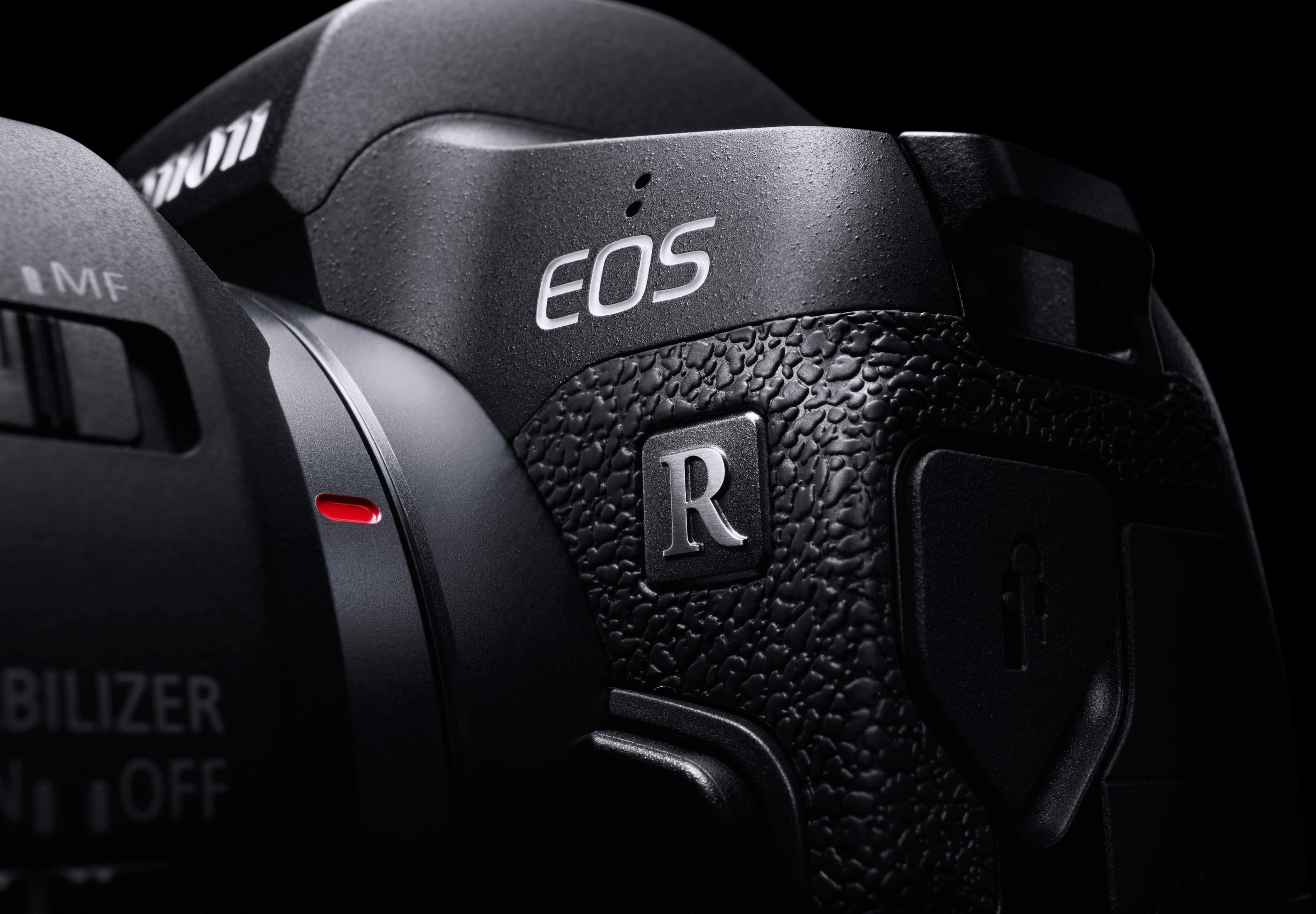 Primo piano di una fotocamera Canon EOS R. Corpo nero con logo argentato 'EOS R' e 'R'.