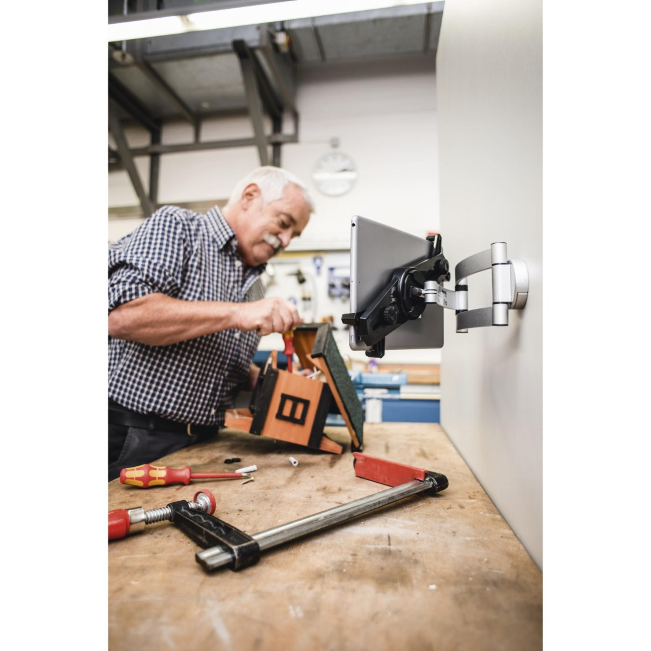Mężczyzna używa narzędzi. Montuje tablet na ramieniu ściennym. Warsztat.