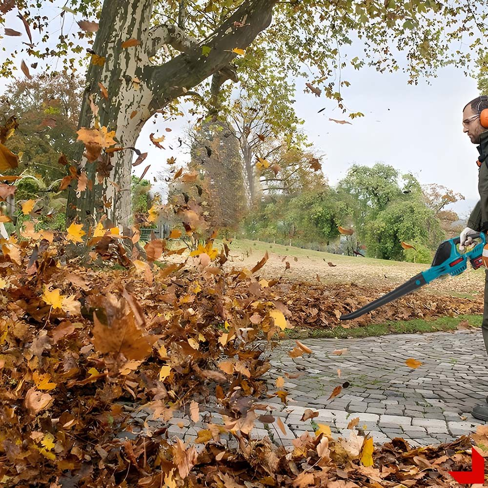Ein Mann bläst Blätter mit einem Laubbläser. Herbstlaub bedeckt einen Backsteinweg und Rasen.