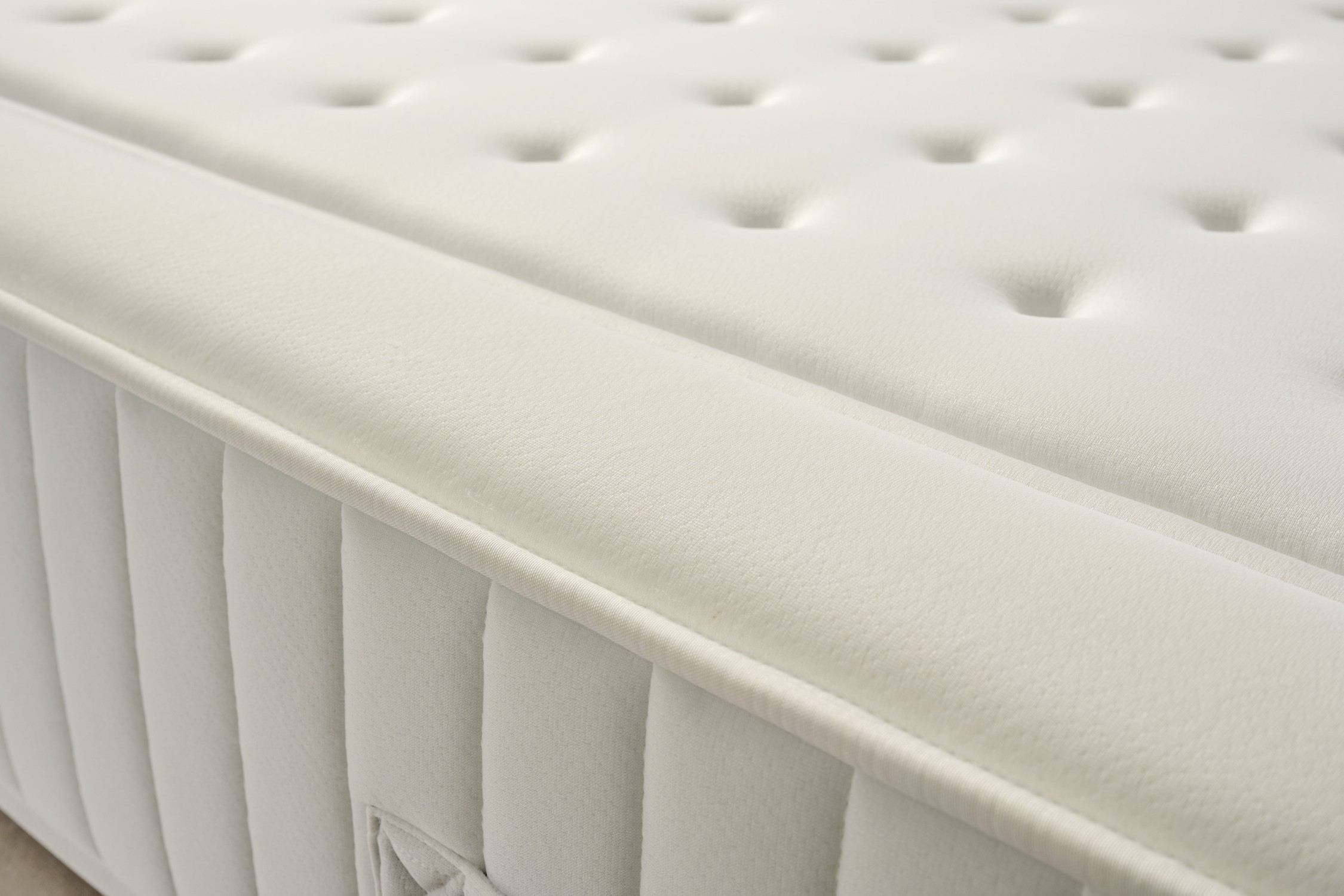 Primer plano de un colchón blanco con botones y borde cosido.