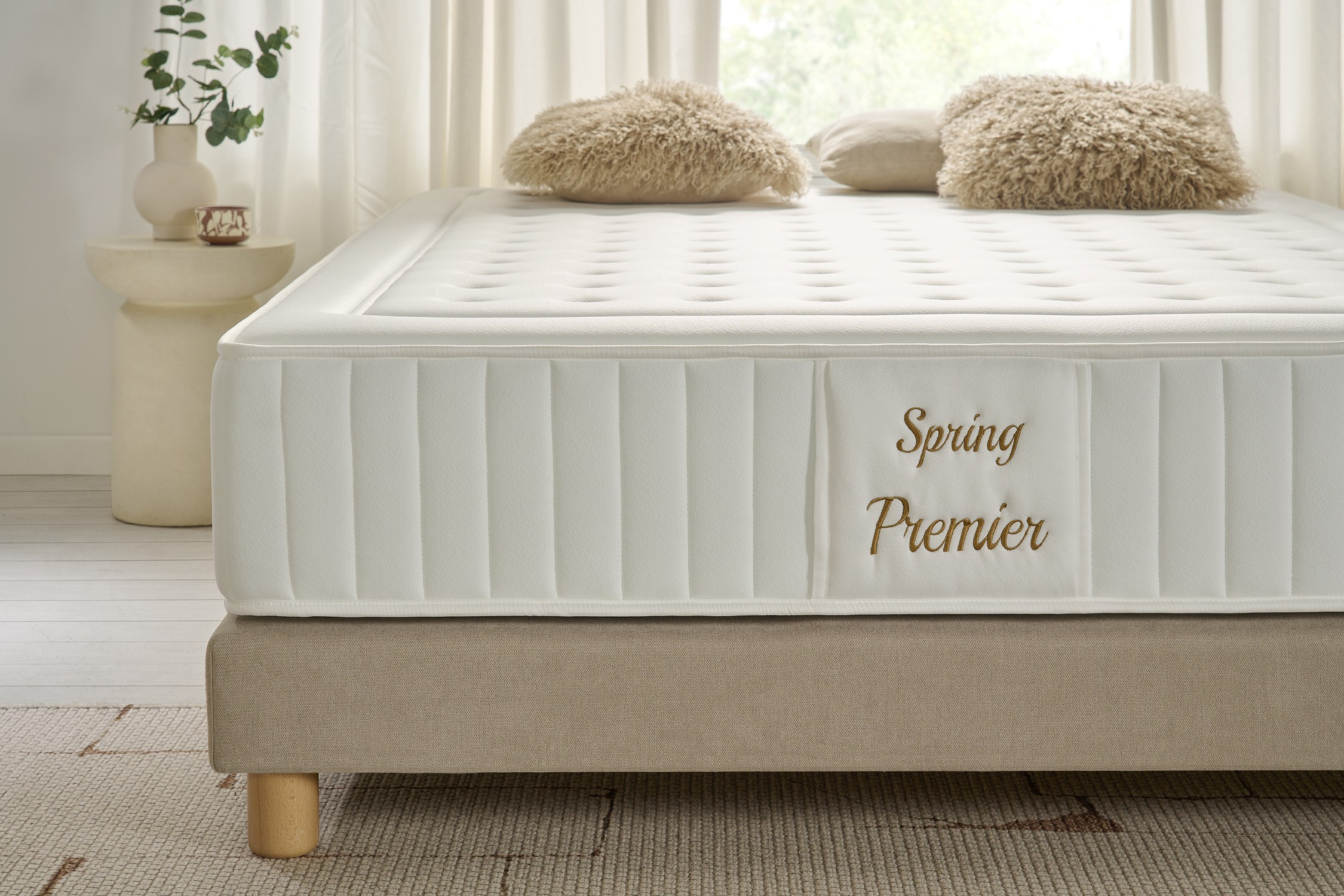Colchón blanco con etiqueta 'Spring Premier', base beige, fondo de ventana.