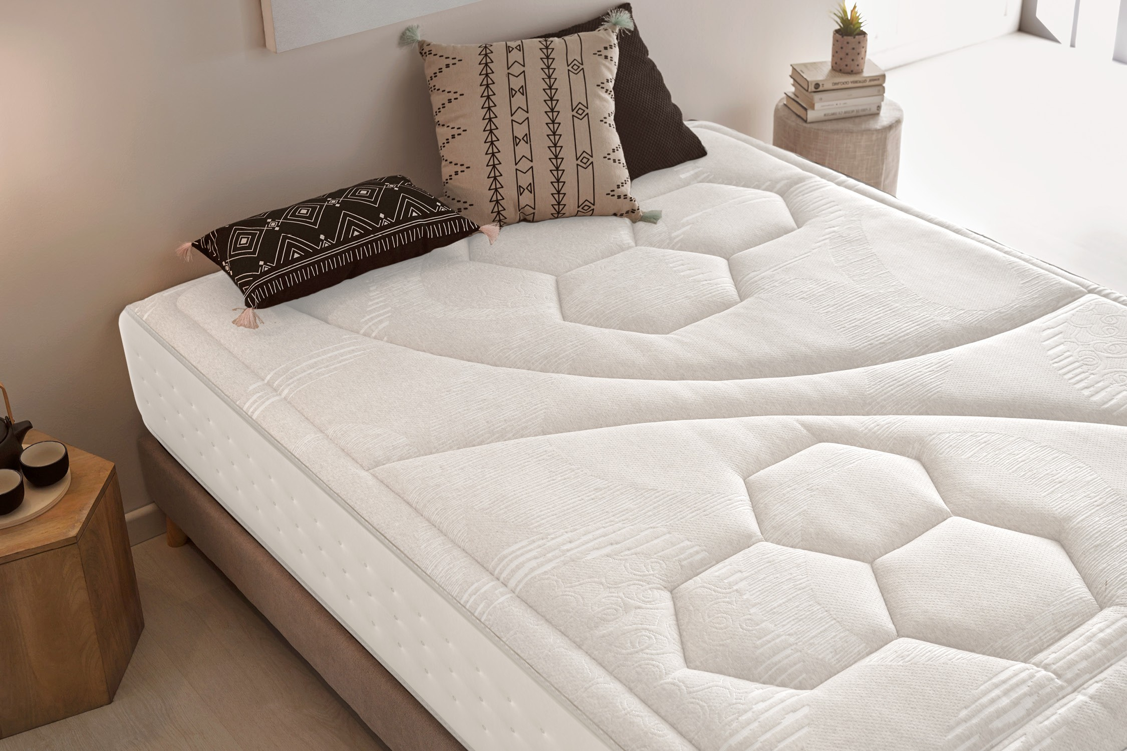 Colchón blanco con almohadas sobre un somier, con fondo neutro.