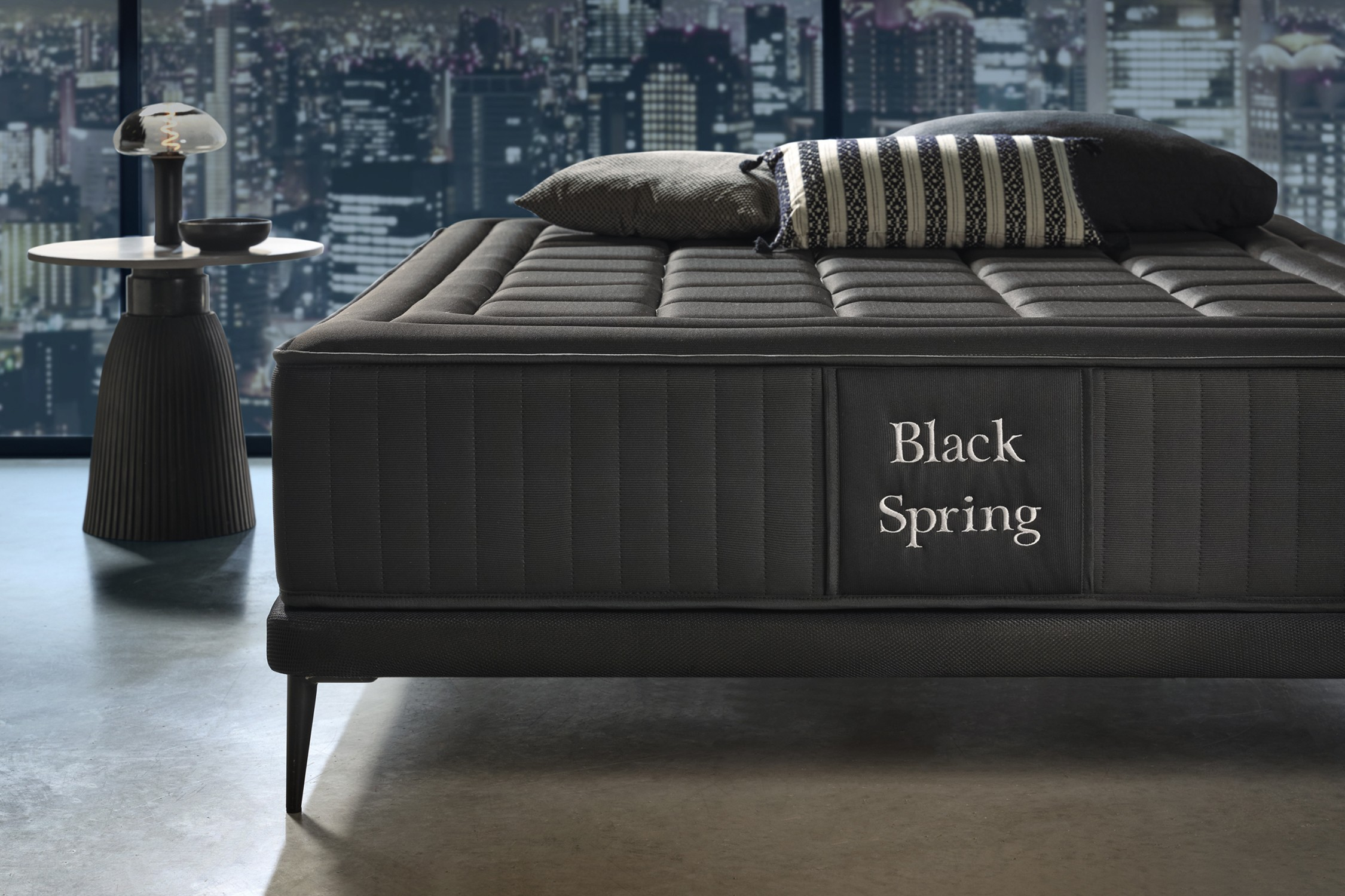 Colchón Black Spring sobre base negra con almohadas y mesa.