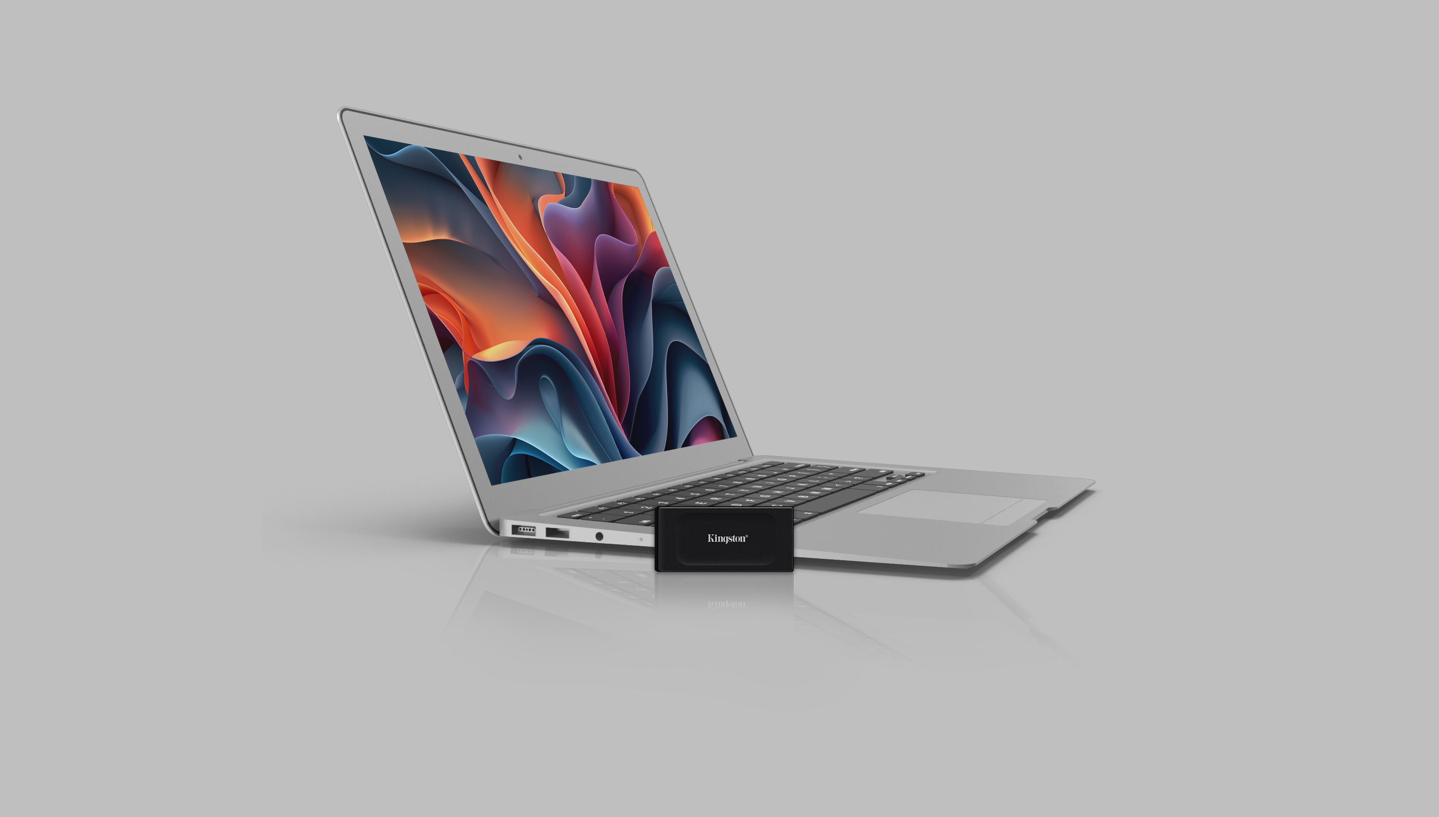 Laptop z zewnętrznym dyskiem SSD Kingston z przodu, na białej powierzchni.