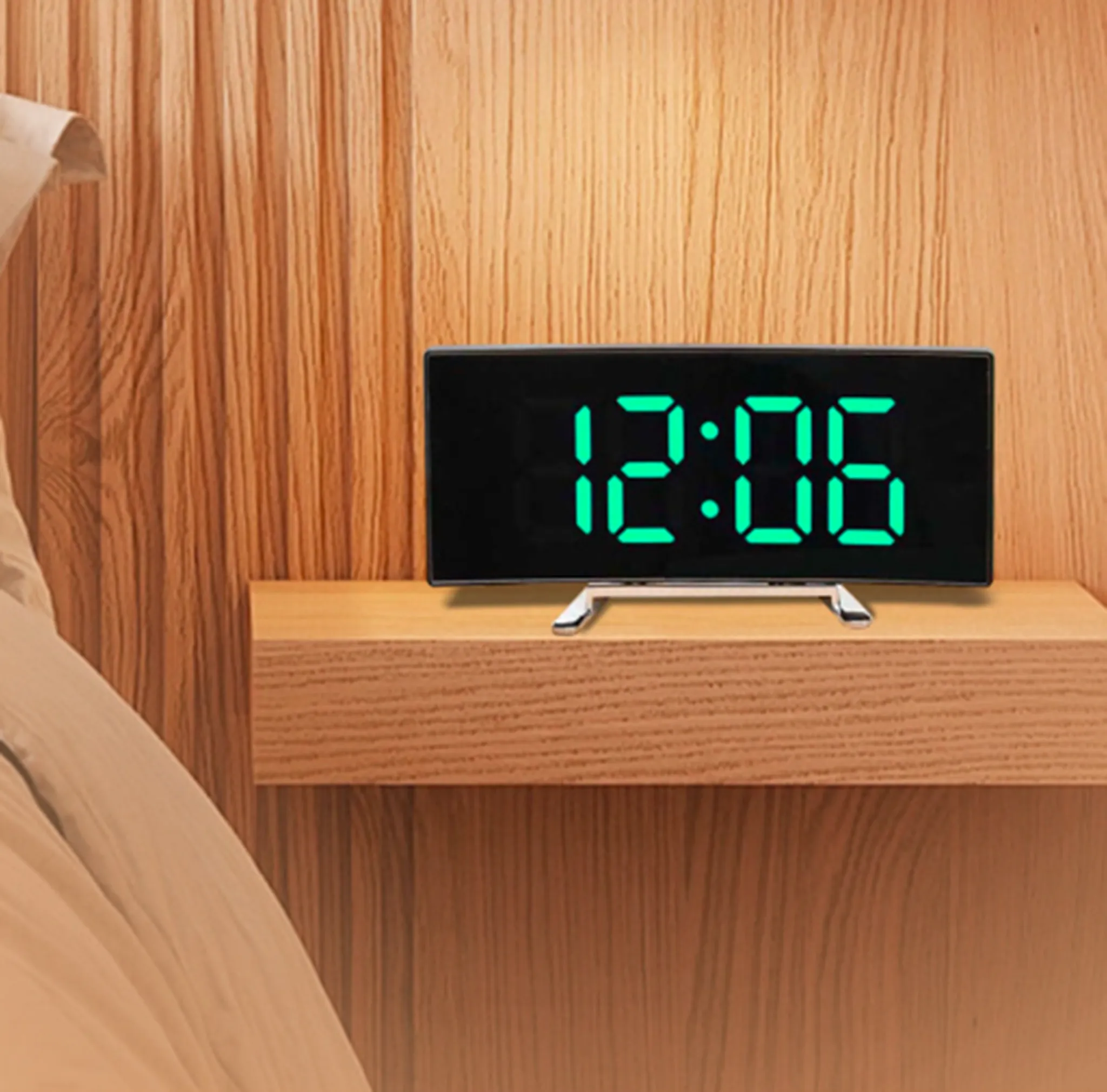 Digitaler Wecker mit grünen Zahlen, die 12:06 anzeigen, auf einer Holzoberfläche in der Nähe eines Bettes platziert.