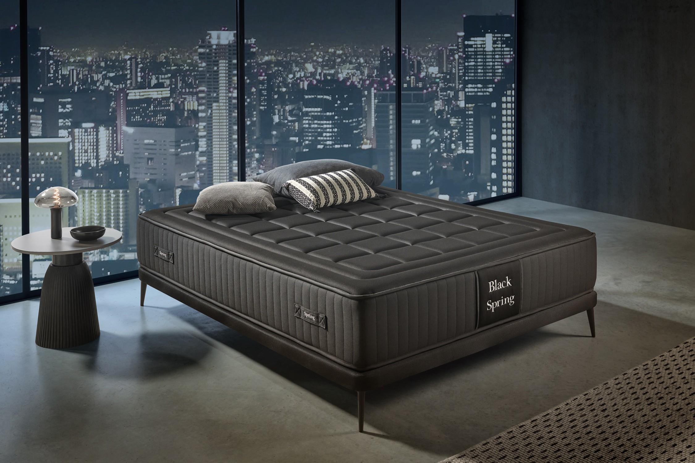 Cama negra en habitación moderna con vistas a la ciudad. Almohadas en la cama. Mesa con lámpara izquierda.