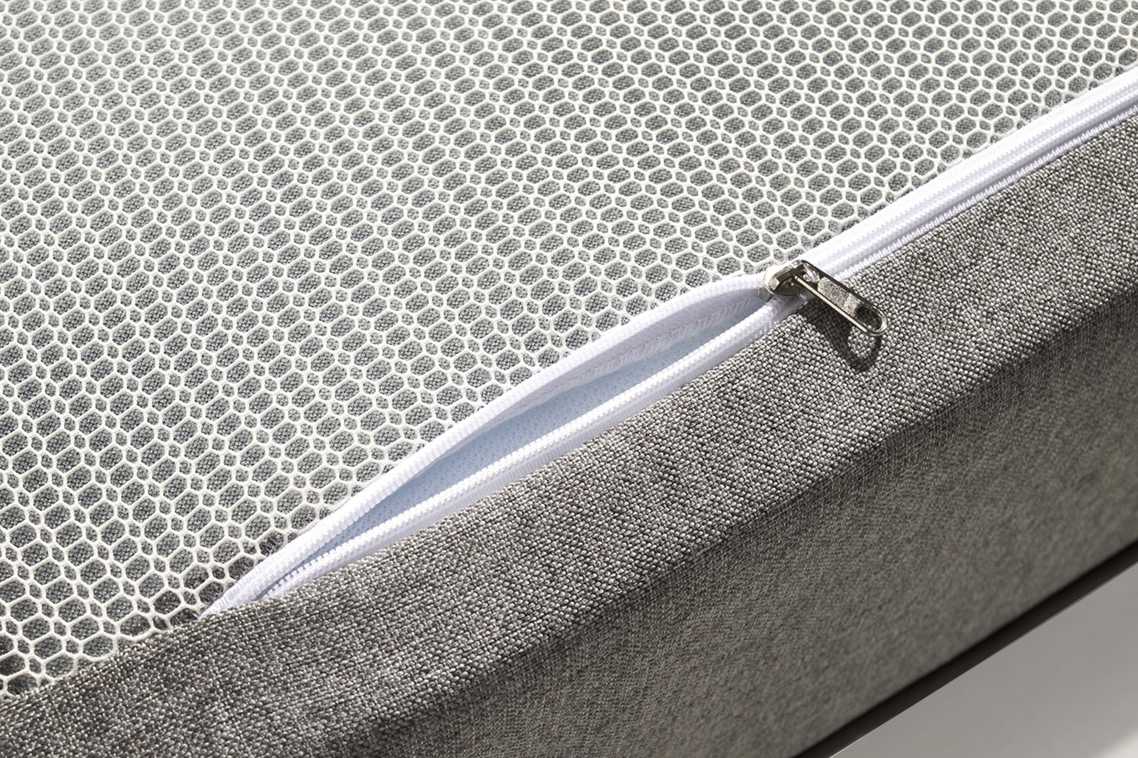 Primer plano de una funda de colchón gris con cremallera blanca, panel de malla de nido de abeja blanco.
