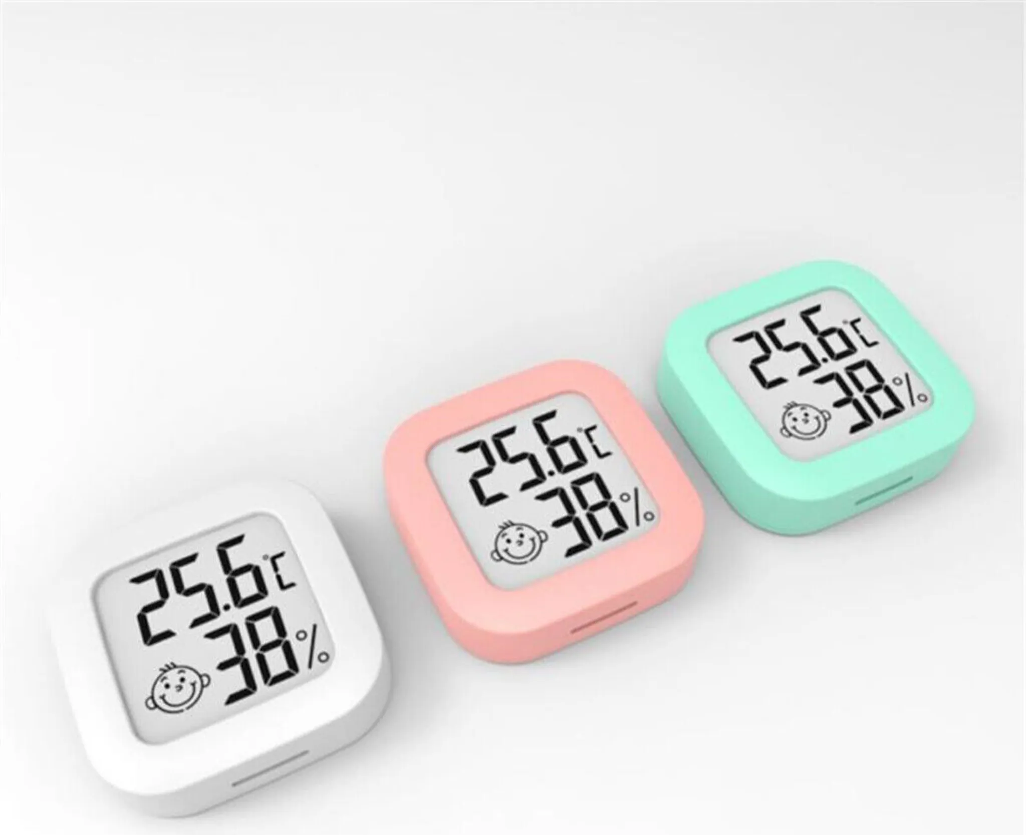 Drei weiße, rosa und grüne quadratische digitale Thermometer, die jeweils Temperatur und Luftfeuchtigkeit anzeigen.