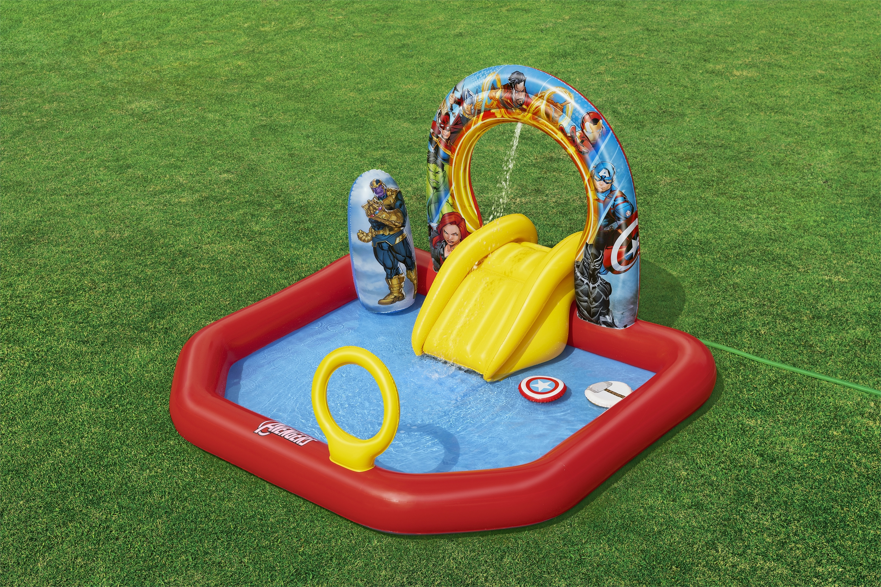 Basen dmuchany w stylu Avengers. Ma zjeżdżalnię, natrysk wody i tarczę Kapitana Ameryki. Zielona trawa.