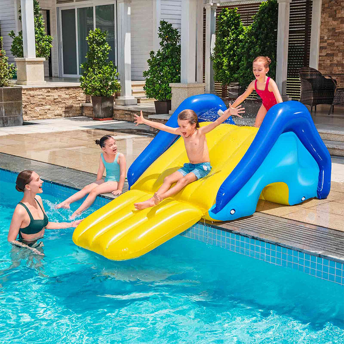 Niños jugando en un tobogán inflable amarillo y azul en una piscina, con una mujer.