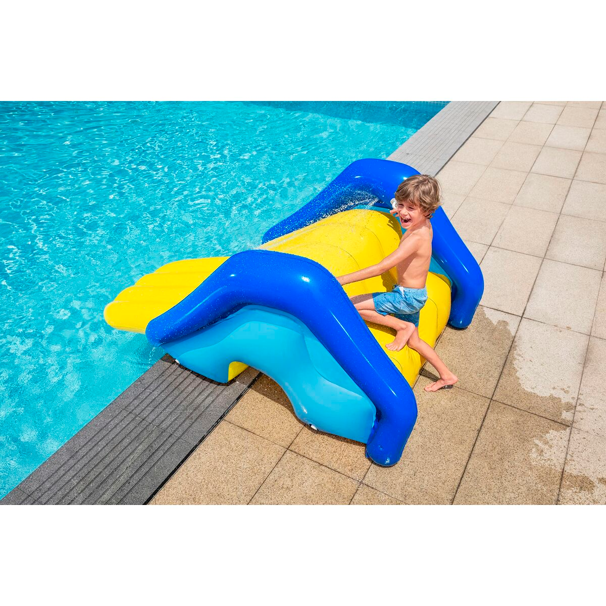 Un niño se desliza por un tobogán inflable amarillo y azul hacia una piscina. Diversión de verano.
