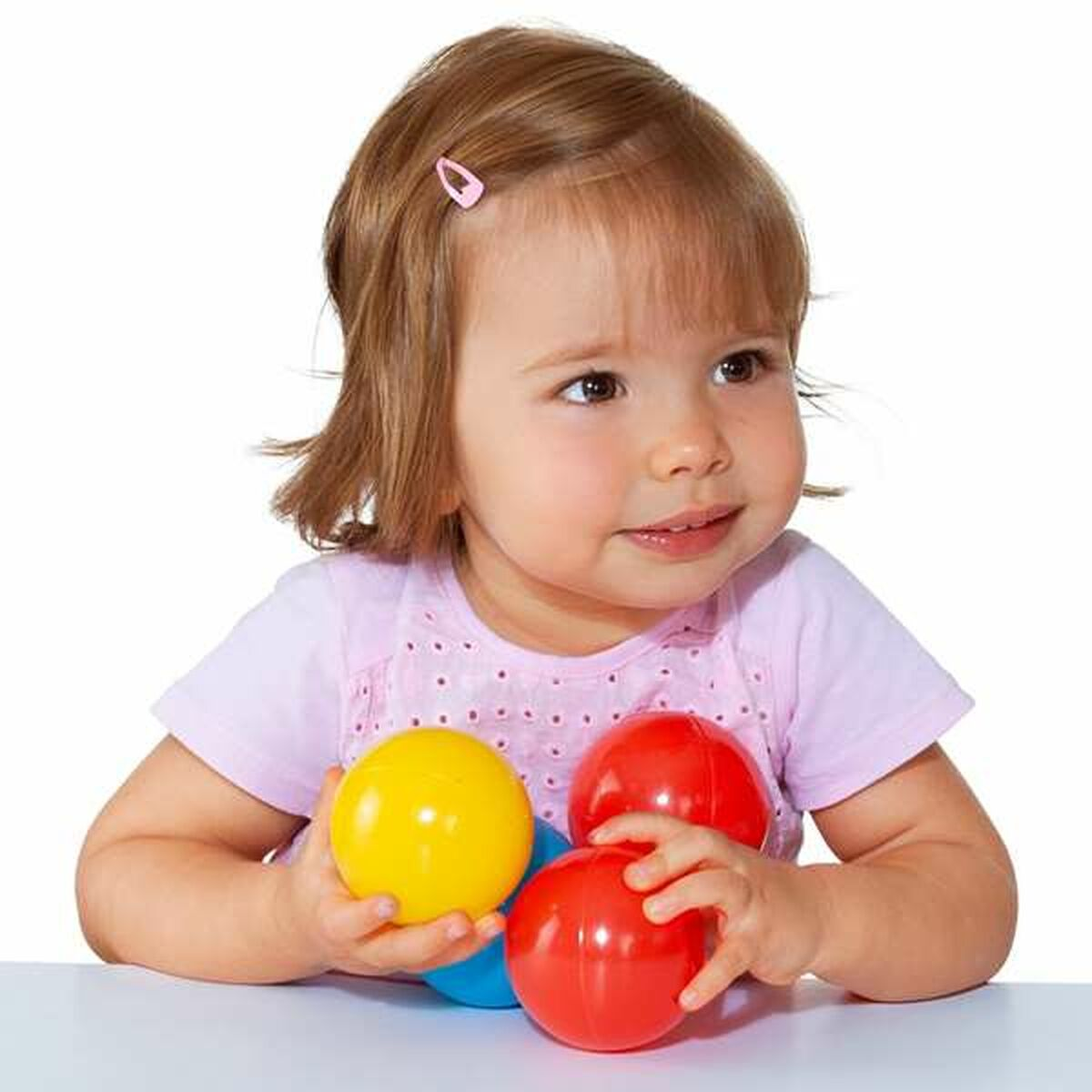 Un bambino piccolo tiene in mano palline colorate, con un fermaglio rosa e una camicia rosa chiaro.