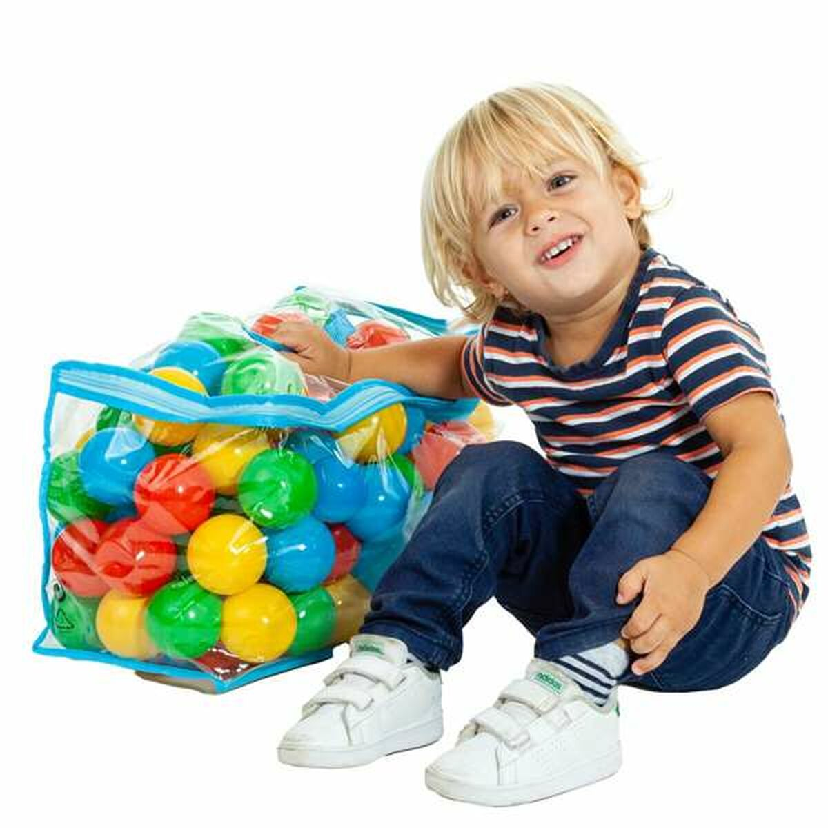 Un bambino piccolo è seduto accanto a una borsa piena di palline colorate. Il bambino sorride e si protende.