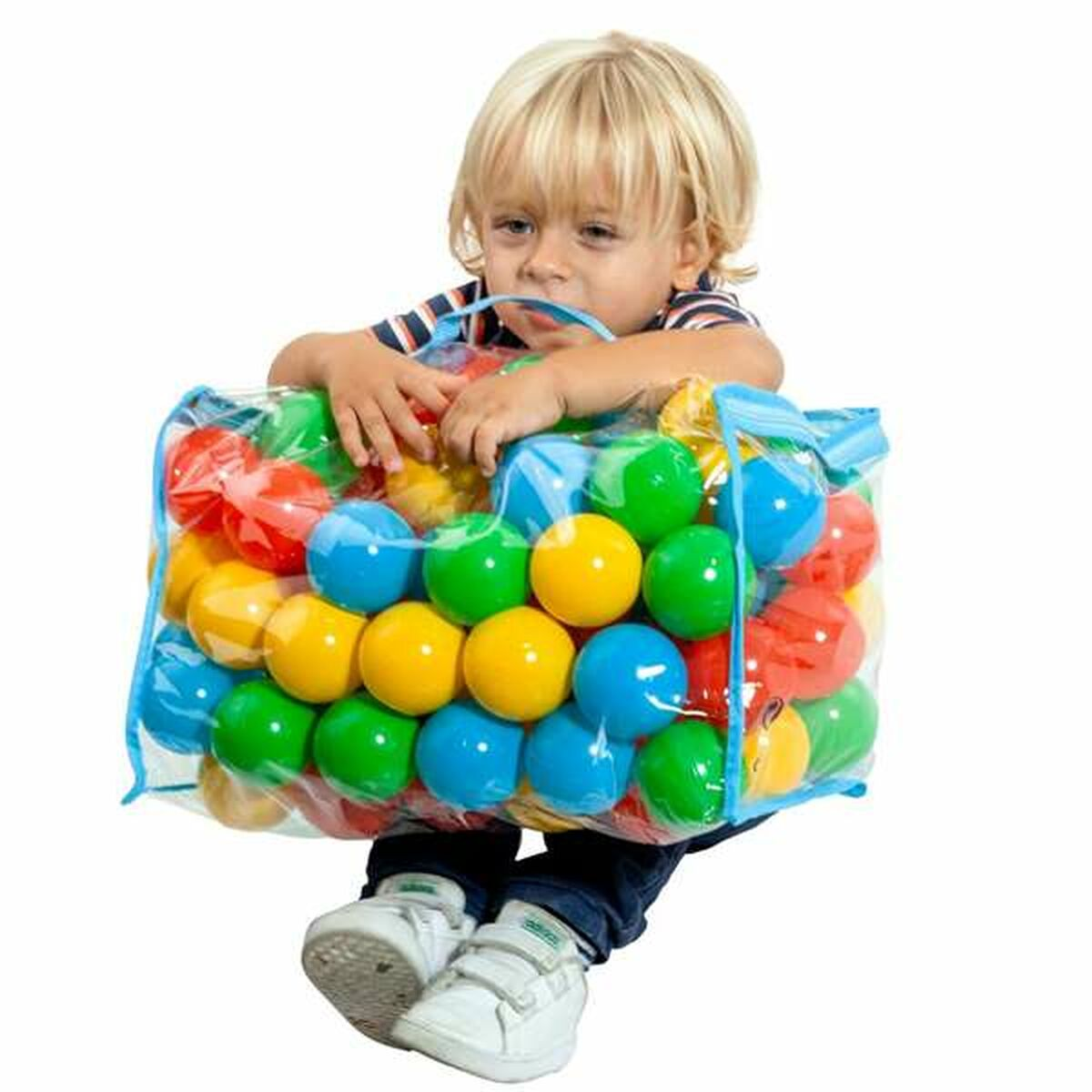 Bambino biondo seduto che tiene un sacco di palline colorate. Sfondo bianco.