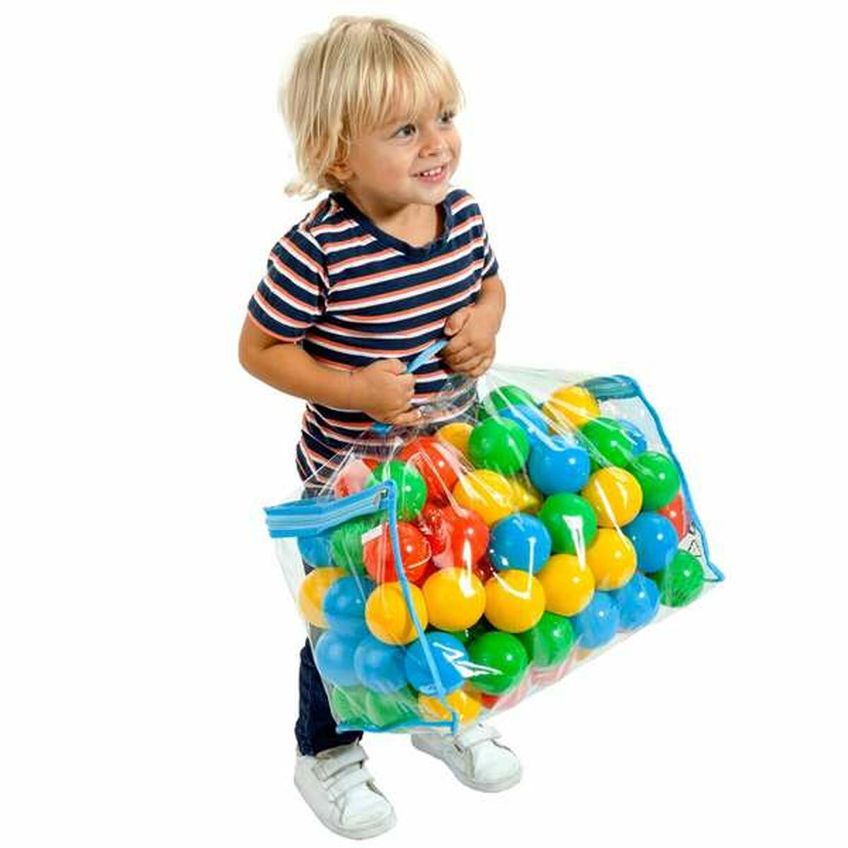 Un ragazzino che tiene in mano una borsa piena di palline colorate. È in piedi e sorride alla fotocamera.