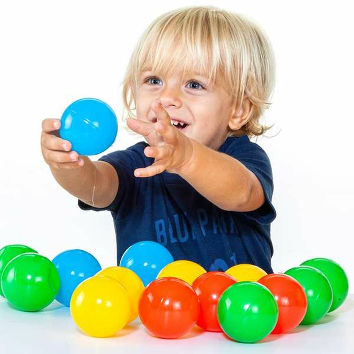 Ragazzo biondo che afferra una palla blu, circondato da palline colorate. Sfondo bianco.