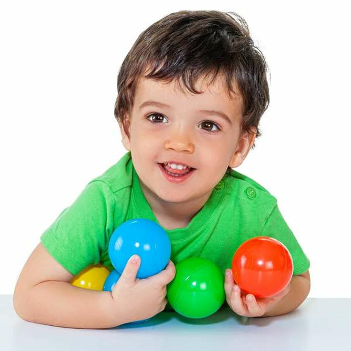 Ragazzo che tiene palle blu, verdi e rosse. Sorridente. Sfondo bianco.