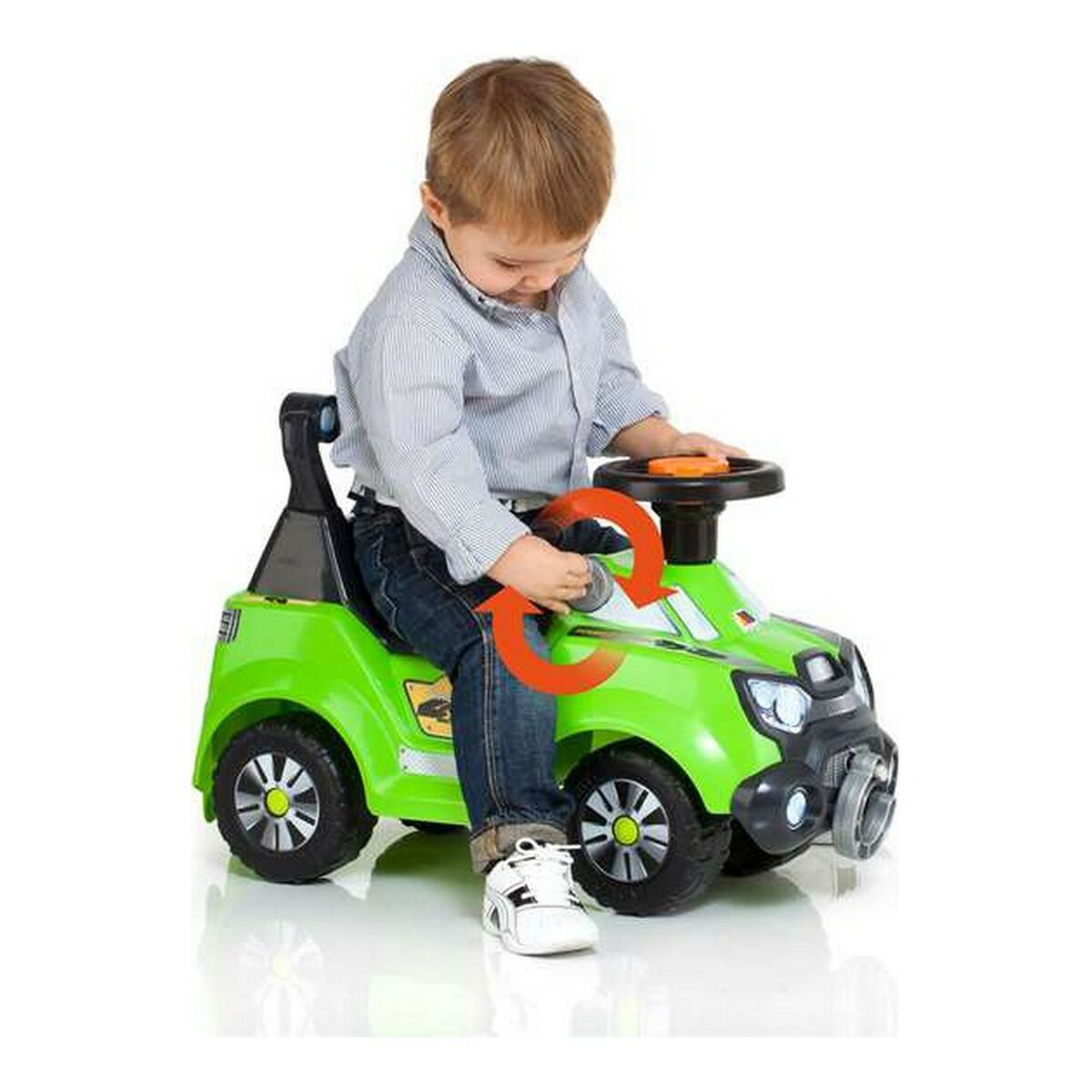 Un ragazzo seduto su un'auto giocattolo verde, guarda il volante. Sfondo bianco.