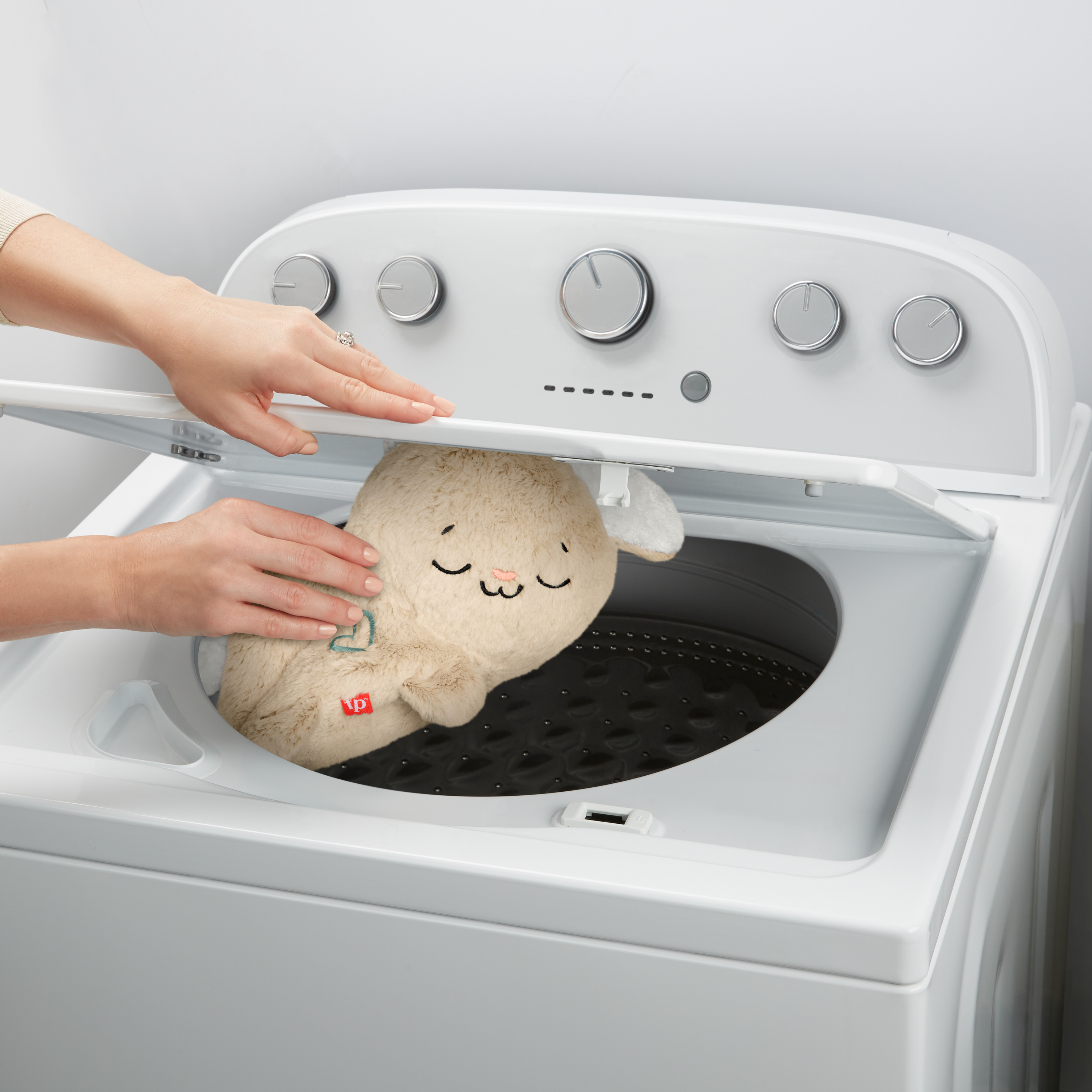 Osoba umieszczająca pluszaka w białej pralce.
