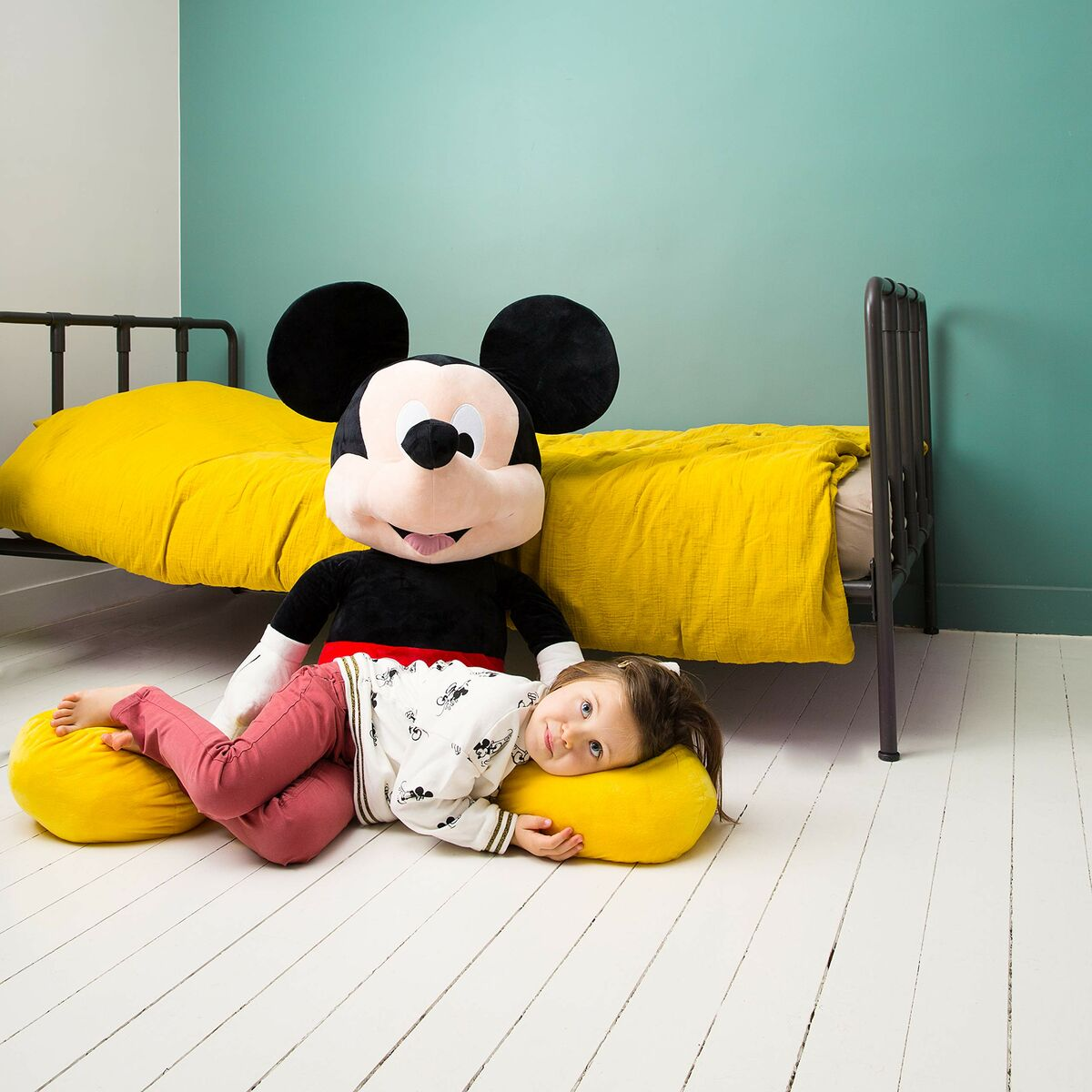 Niño acostado sobre almohada amarilla. Peluche de Mickey Mouse. Fondo de pared verde.