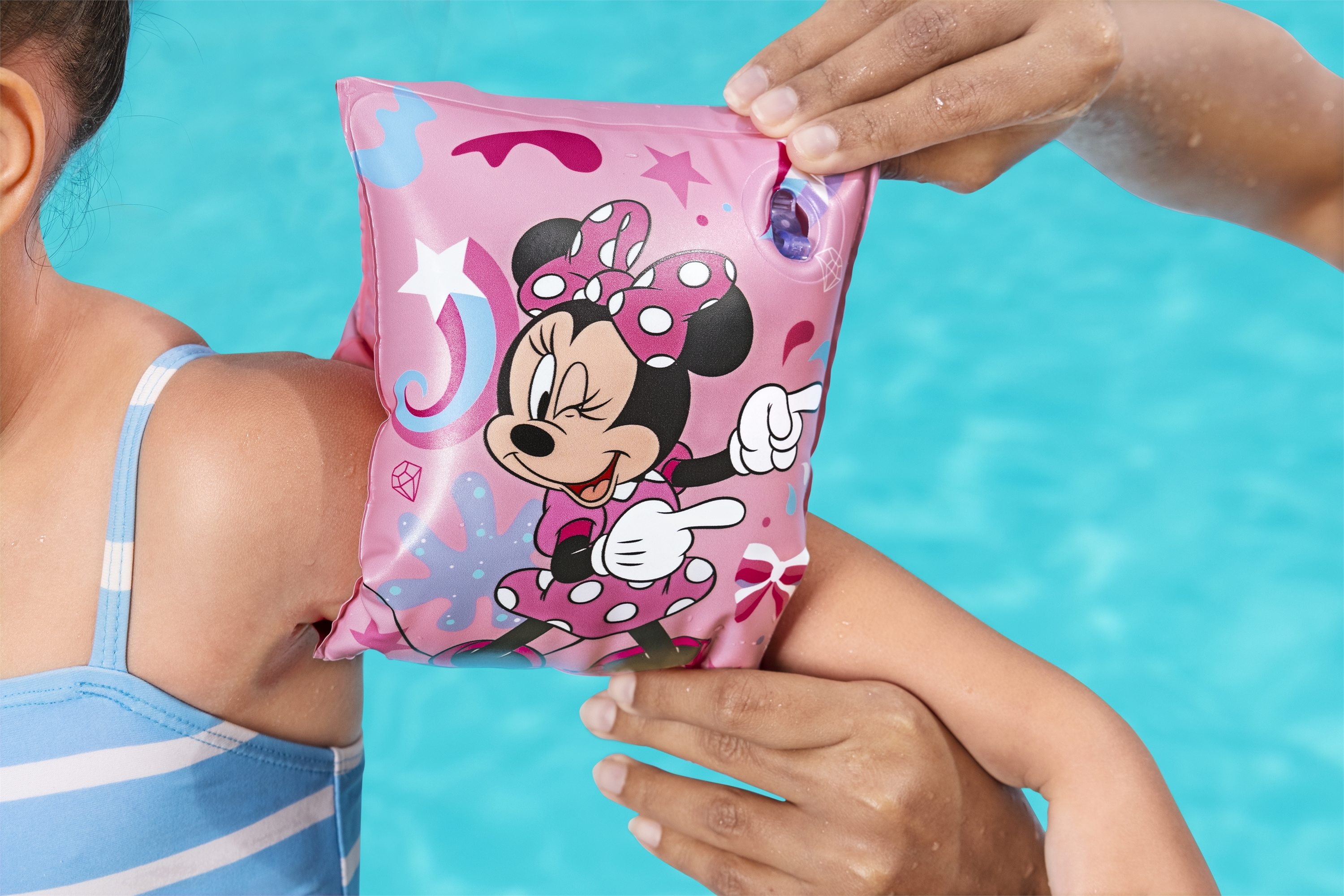 Una persona pone un flotador de brazo rosa de Minnie Mouse a un niño en una piscina.