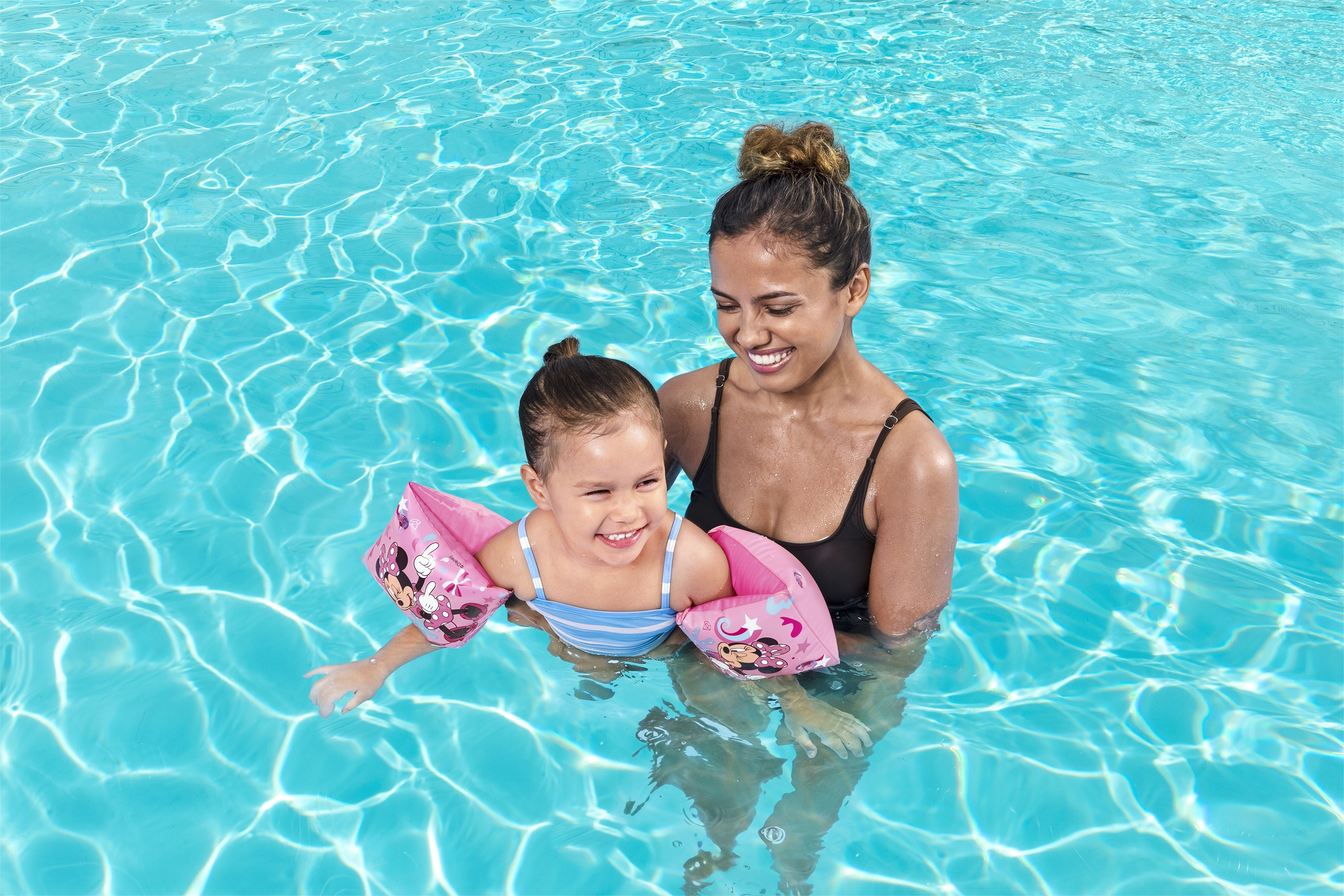 Una mujer y una niña en una piscina con flotadores de brazo de Minnie Mouse, sonriendo.