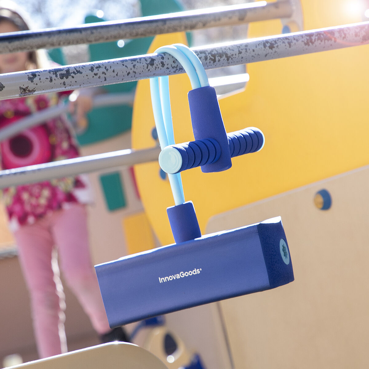 Un pogo stick azul y celeste está sujeto a una barra de metal en un parque infantil, con una niña al fondo.