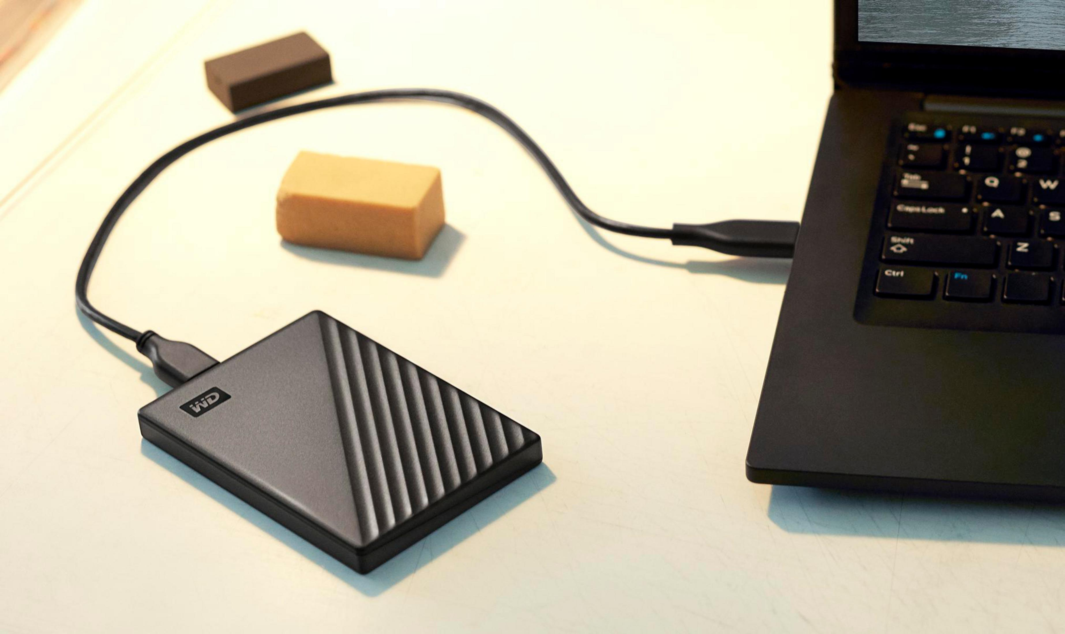 Czarny zewnętrzny dysk twardy podłączony do laptopa na białym biurku, z dwoma małymi brązowymi klockami.