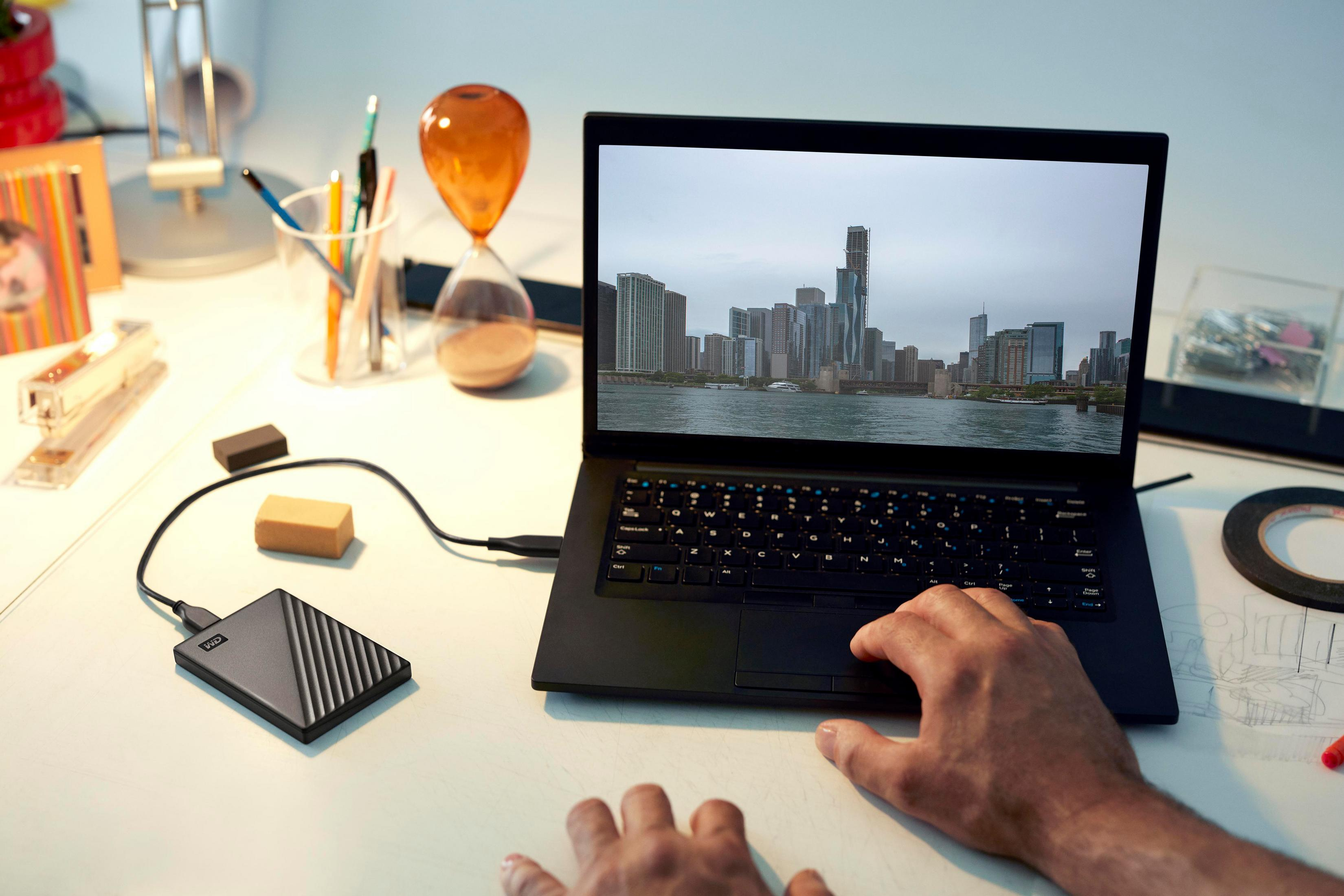 Laptop wyświetlający panoramę miasta, podłączony do czarnego zewnętrznego dysku twardego na biurku.