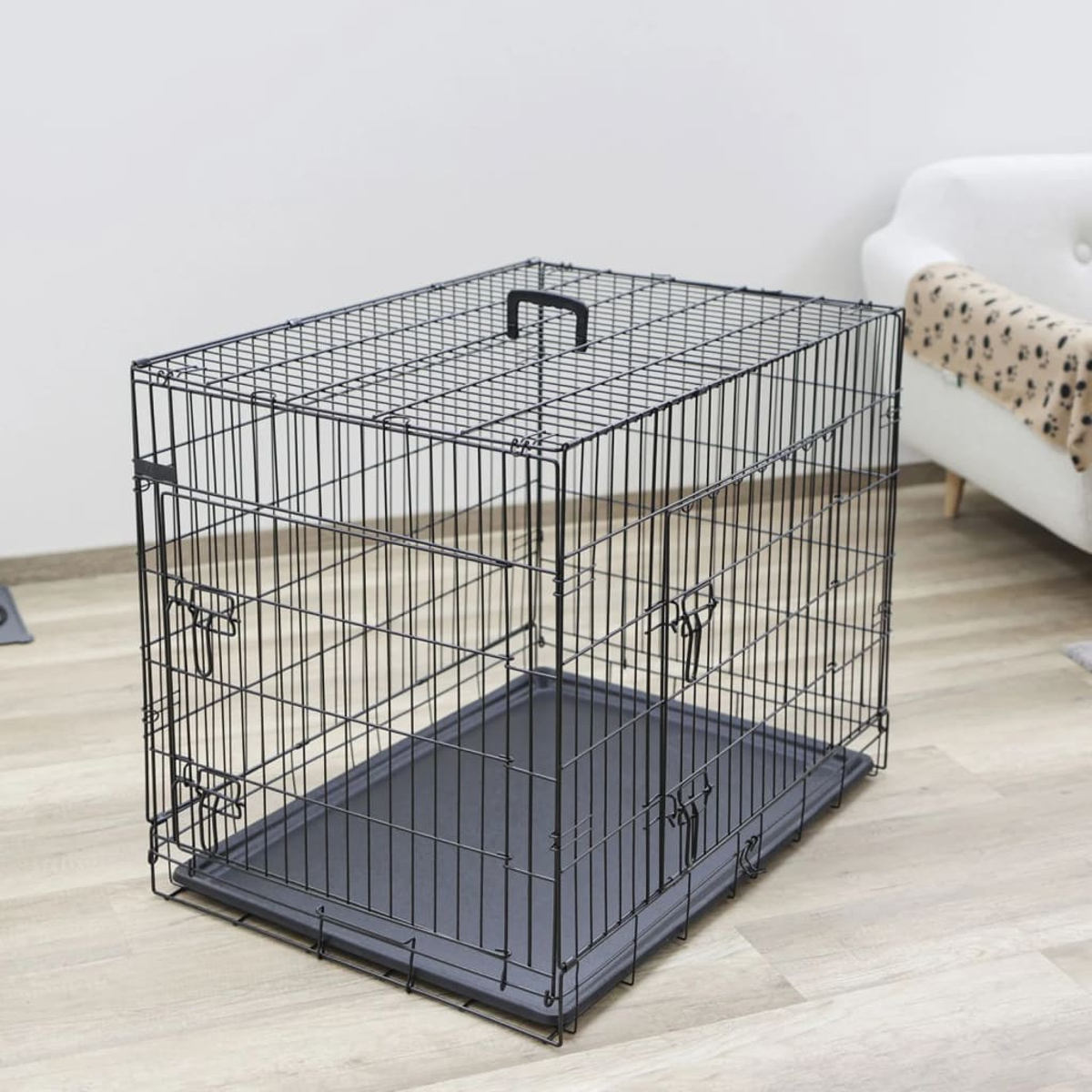 Eine schwarze Hunde-Drahtbox mit schwarzem Kunststoffboden, auf einem hellen Holzboden.